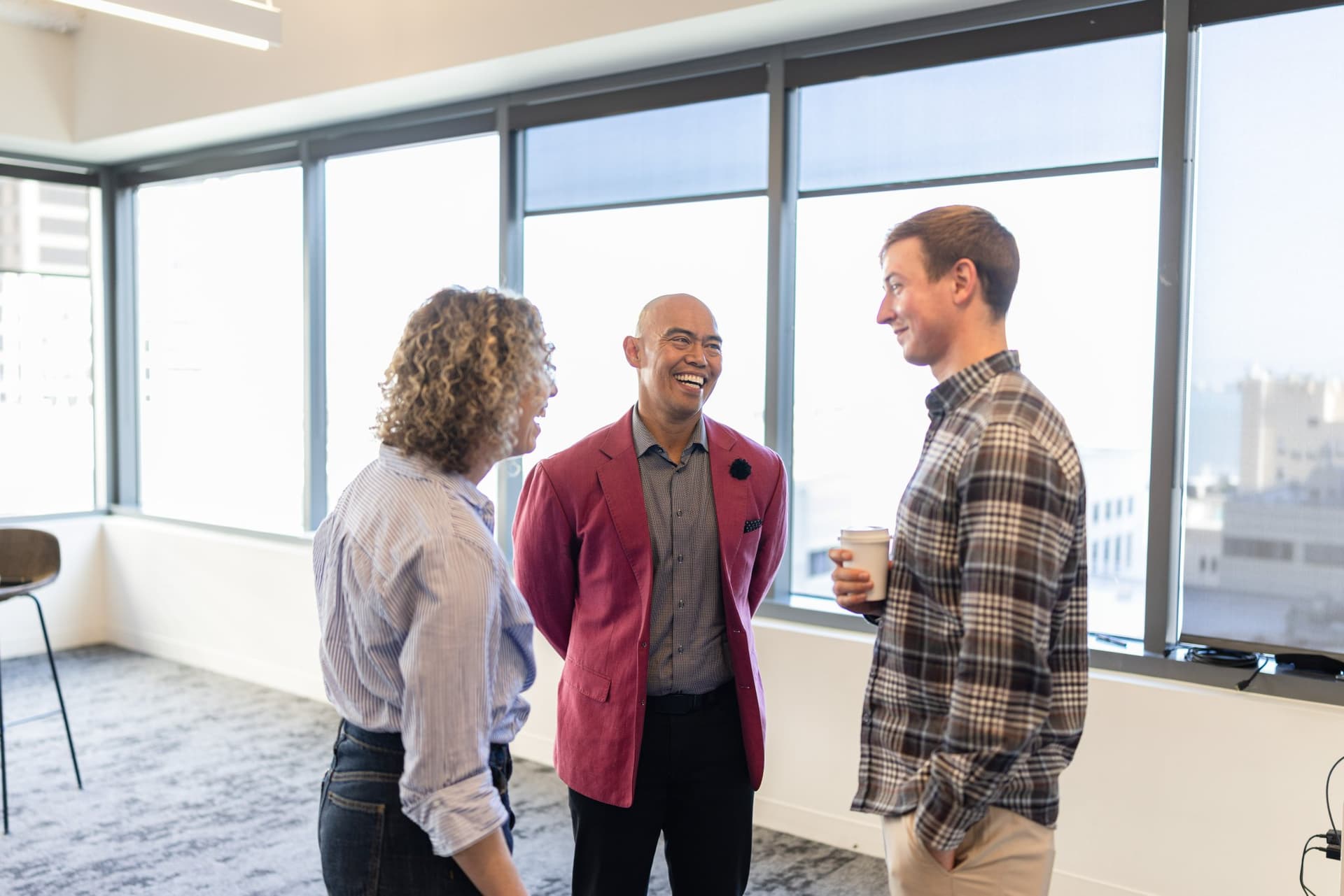 Dean Quiambao and Drew Armanino talking with a guest by the window at Airwallex's Beyond the Hype: AI and the Future of Finance breakfast fireside chat at the Airwallex San Francisco office by JY Studio