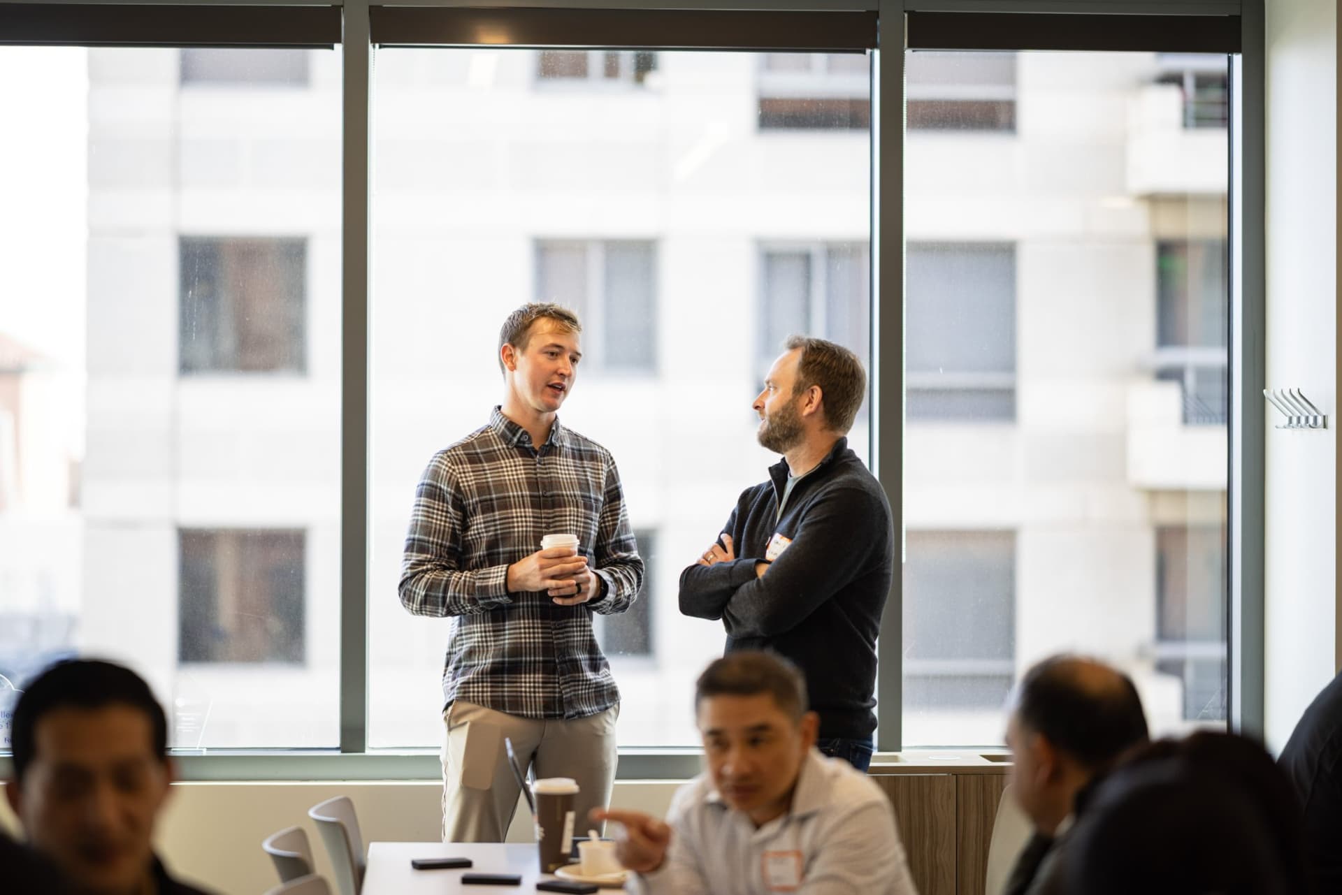 Drew Armanino chatting with a guest by the window over coffee at Airwallex's Beyond the Hype: AI and the Future of Finance breakfast fireside chat at the Airwallex San Francisco office by JY Studio
