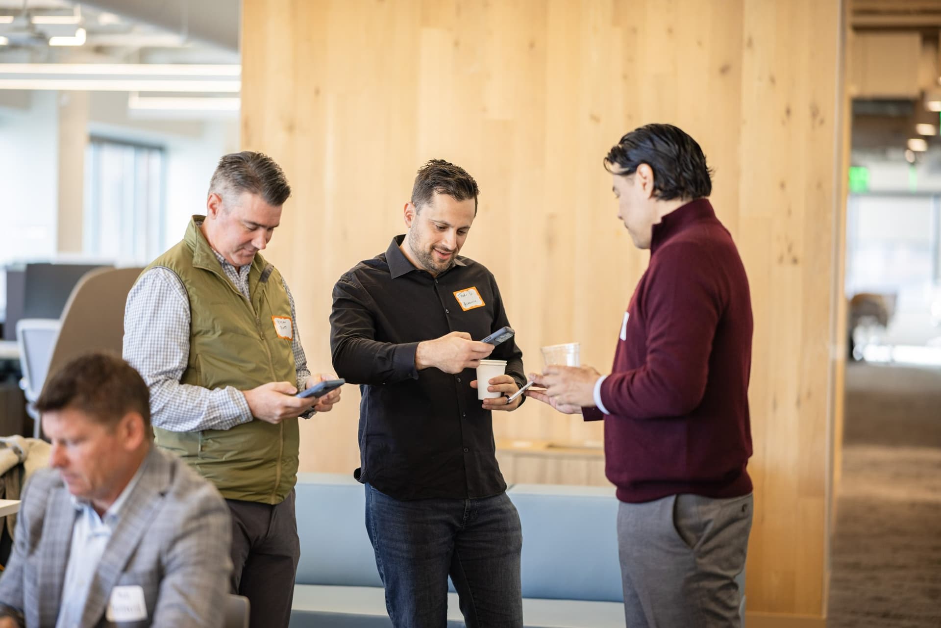 Three finance leaders exchanging contacts on their phones at Airwallex's Beyond the Hype: AI and the Future of Finance breakfast fireside chat at the Airwallex San Francisco office by JY Studio