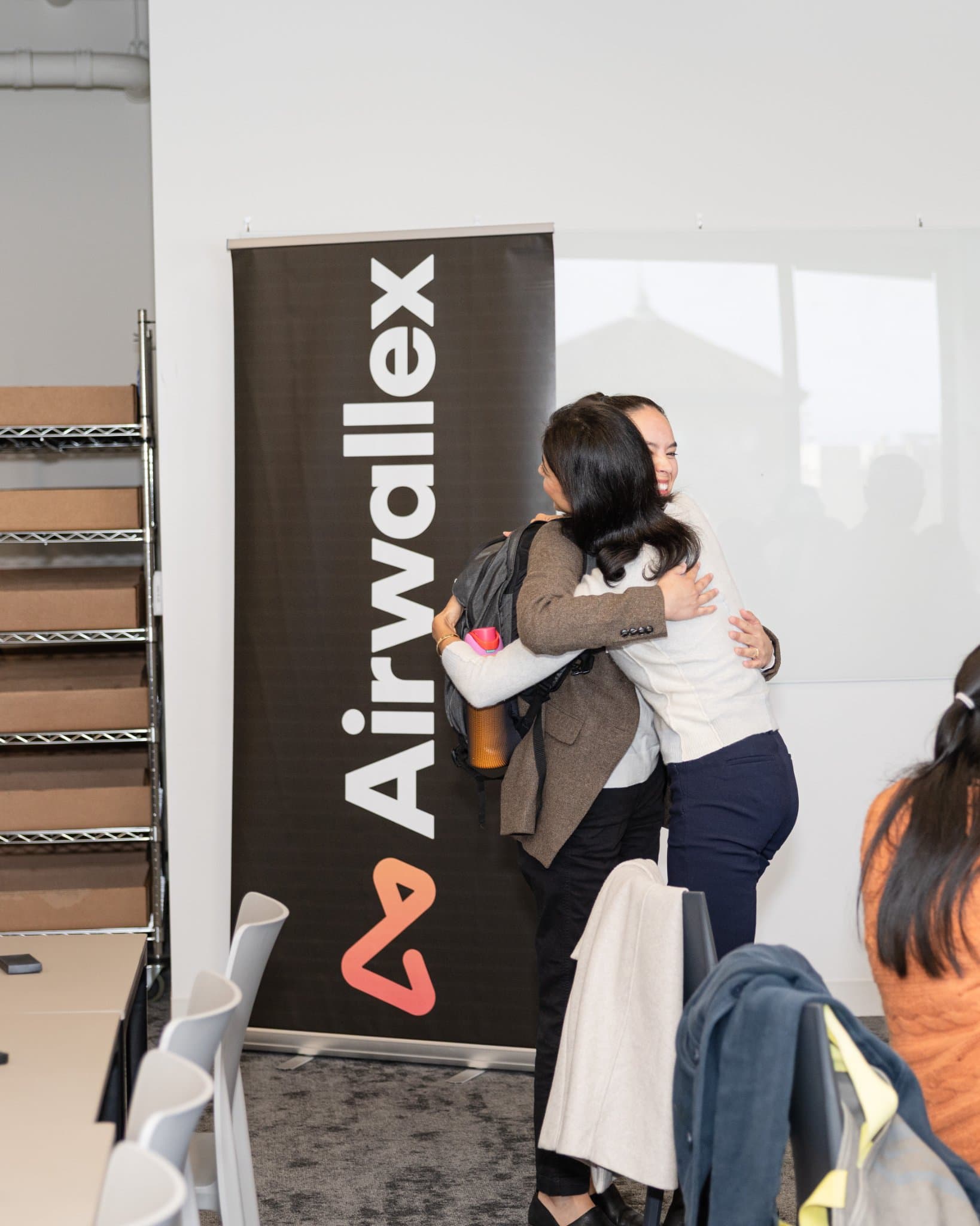 Two guests hugging beside the Airwallex banner at Airwallex's Beyond the Hype: AI and the Future of Finance breakfast fireside chat at the Airwallex San Francisco office by JY Studio