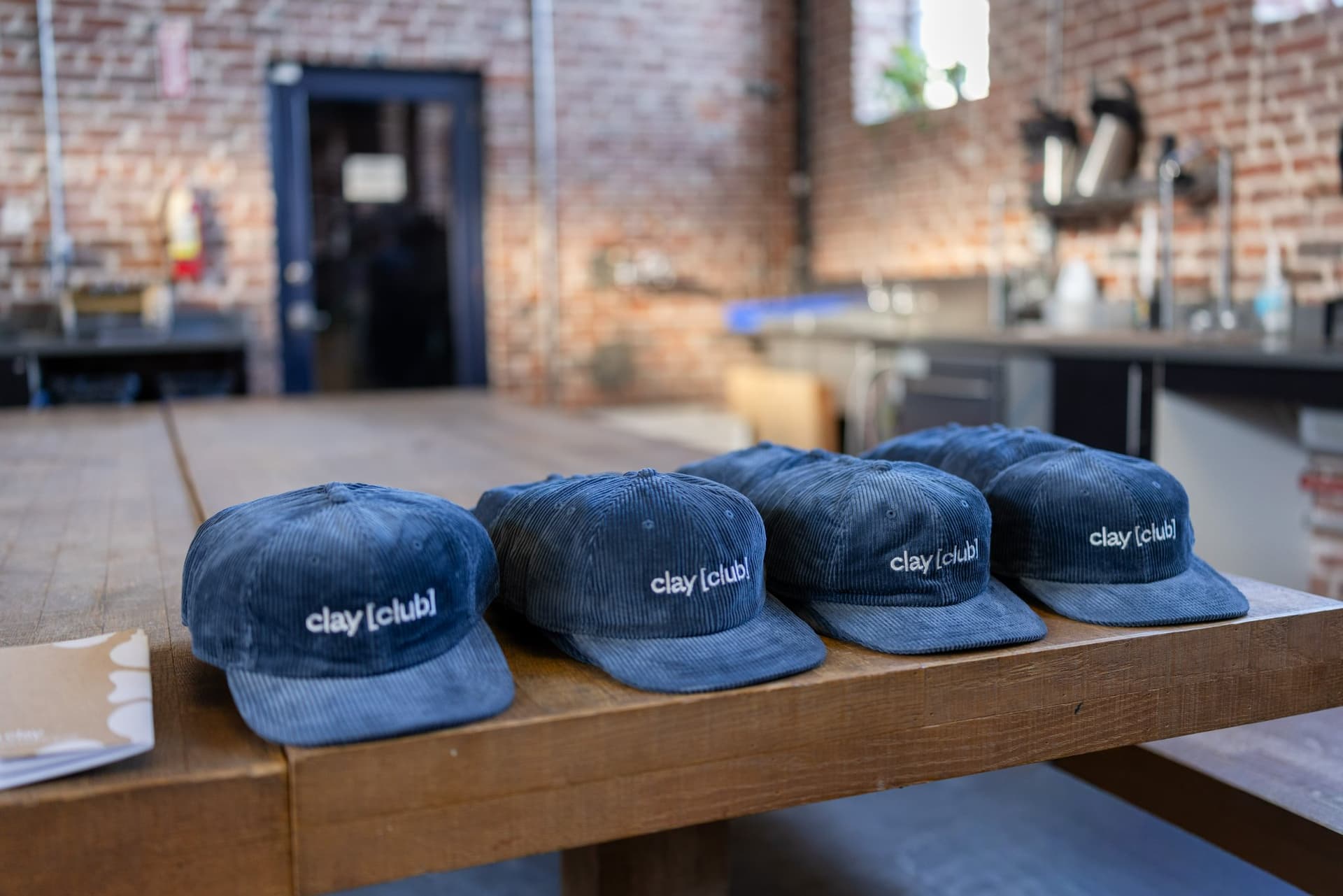 Clay Club corduroy caps laid out on a wooden table at Clay's Breaking the Mold community networking event during SF Tech Week 2026 in San Francisco by JY Studio