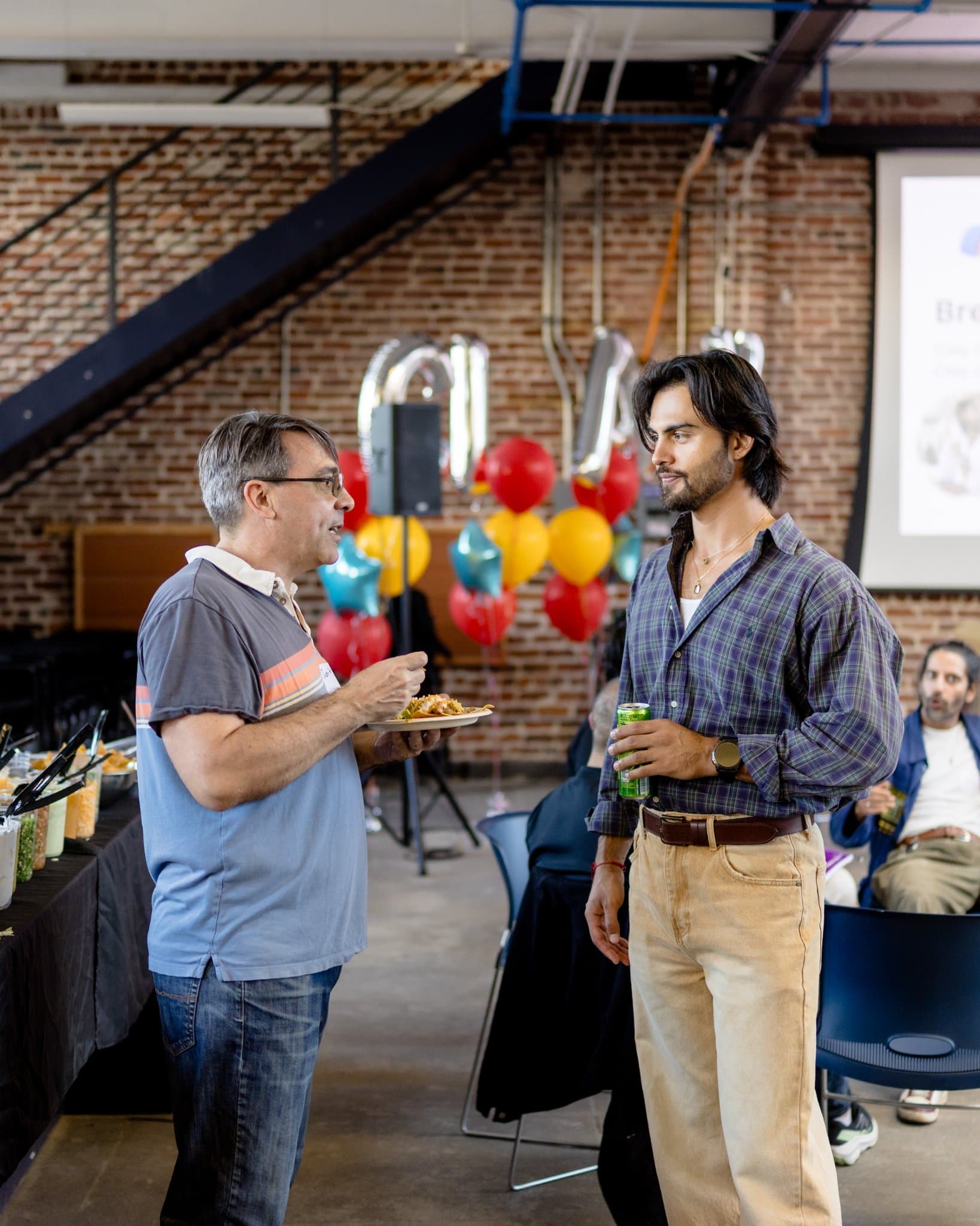Two guests talking over plates and drinks by the buffet at Clay's Breaking the Mold community networking event during SF Tech Week 2026 in San Francisco by JY Studio