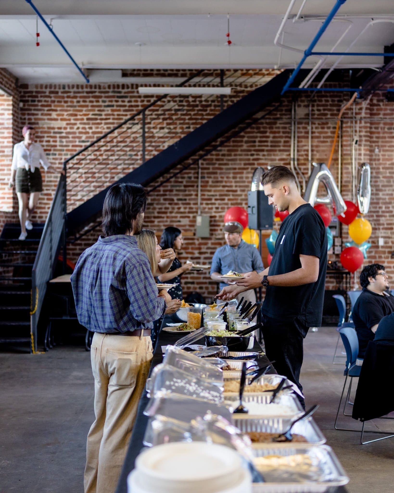 Guests lining up along the buffet table under the staircase at Clay's Breaking the Mold community networking event during SF Tech Week 2026 in San Francisco by JY Studio
