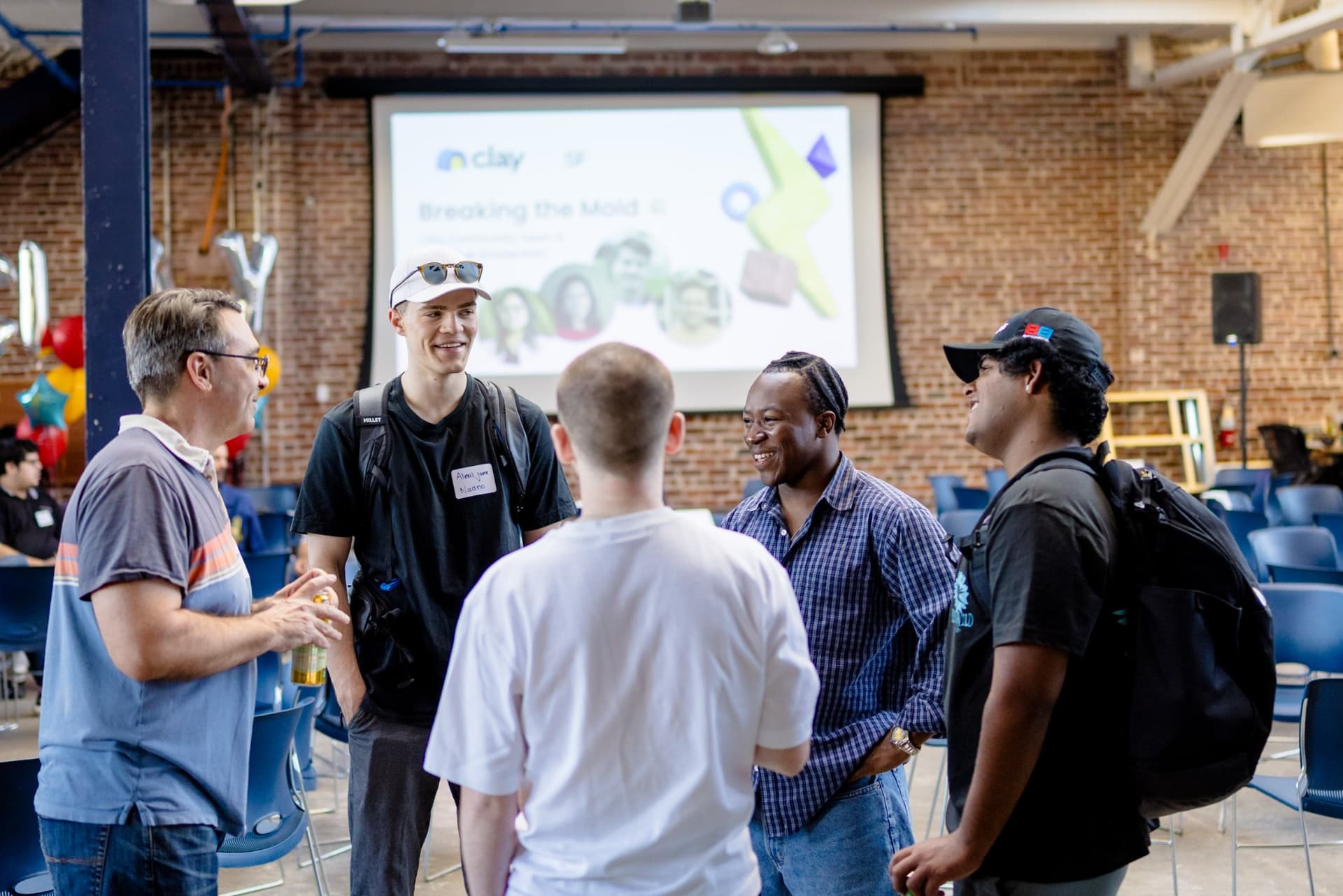 Group of GTM builders talking in front of the Breaking the Mold slide at Clay's Breaking the Mold community networking event during SF Tech Week 2026 in San Francisco by JY Studio