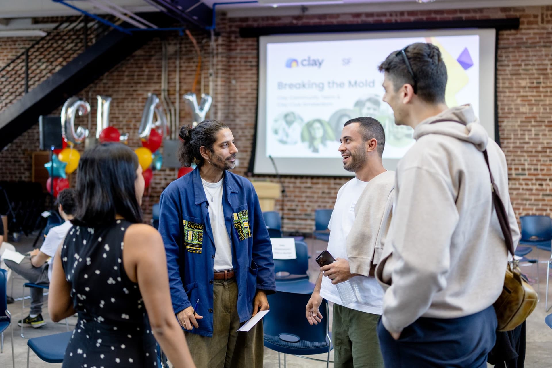 Guests laughing together beside the CLAY balloons and welcome slide at Clay's Breaking the Mold community networking event during SF Tech Week 2026 in San Francisco by JY Studio