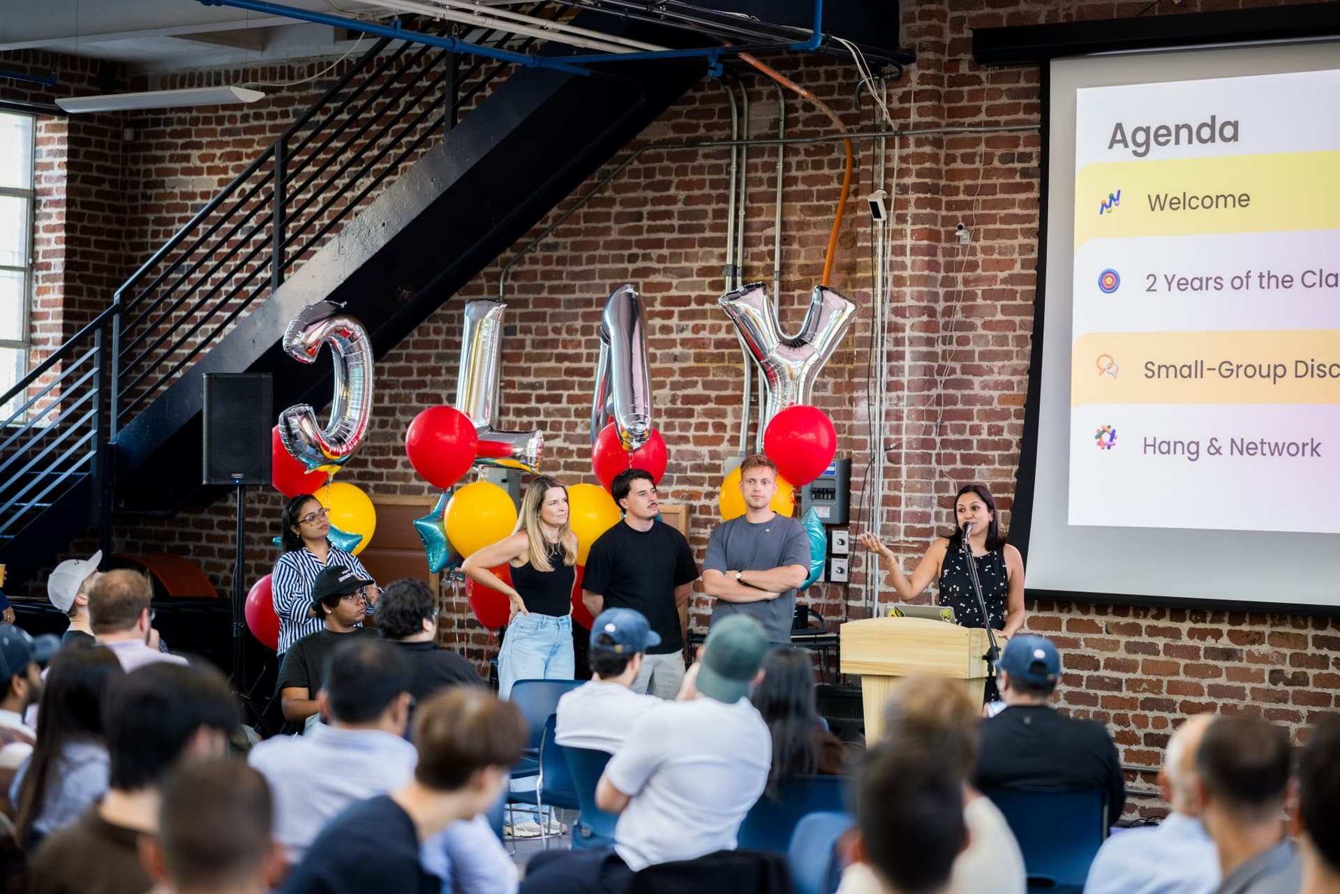 Host opening the evening at the podium with the agenda on screen at Clay's Breaking the Mold community networking event during SF Tech Week 2026 in San Francisco by JY Studio