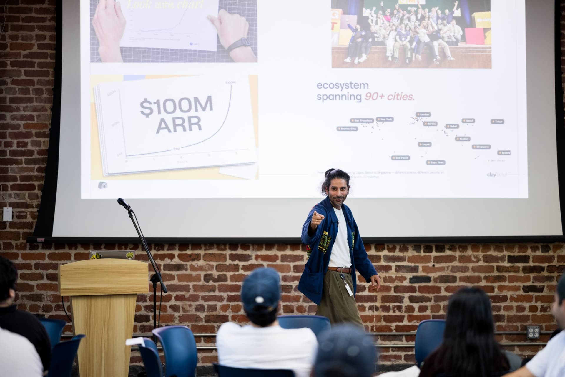 Clay Community lead presenting the $100M ARR milestone slide at Clay's Breaking the Mold community networking event during SF Tech Week 2026 in San Francisco by JY Studio