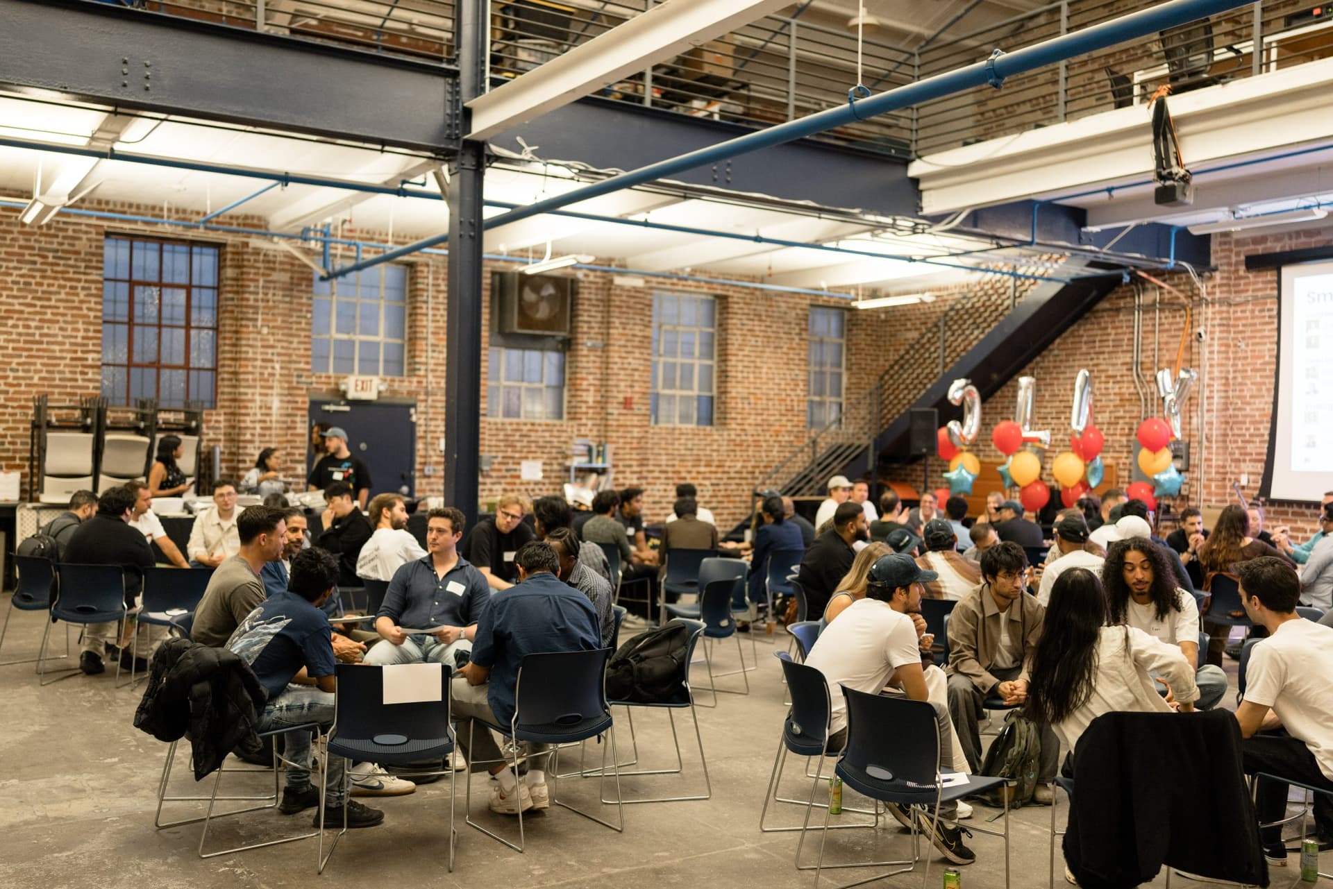 Wide view of the warehouse filled with small-group discussion circles at Clay's Breaking the Mold community networking event during SF Tech Week 2026 in San Francisco by JY Studio