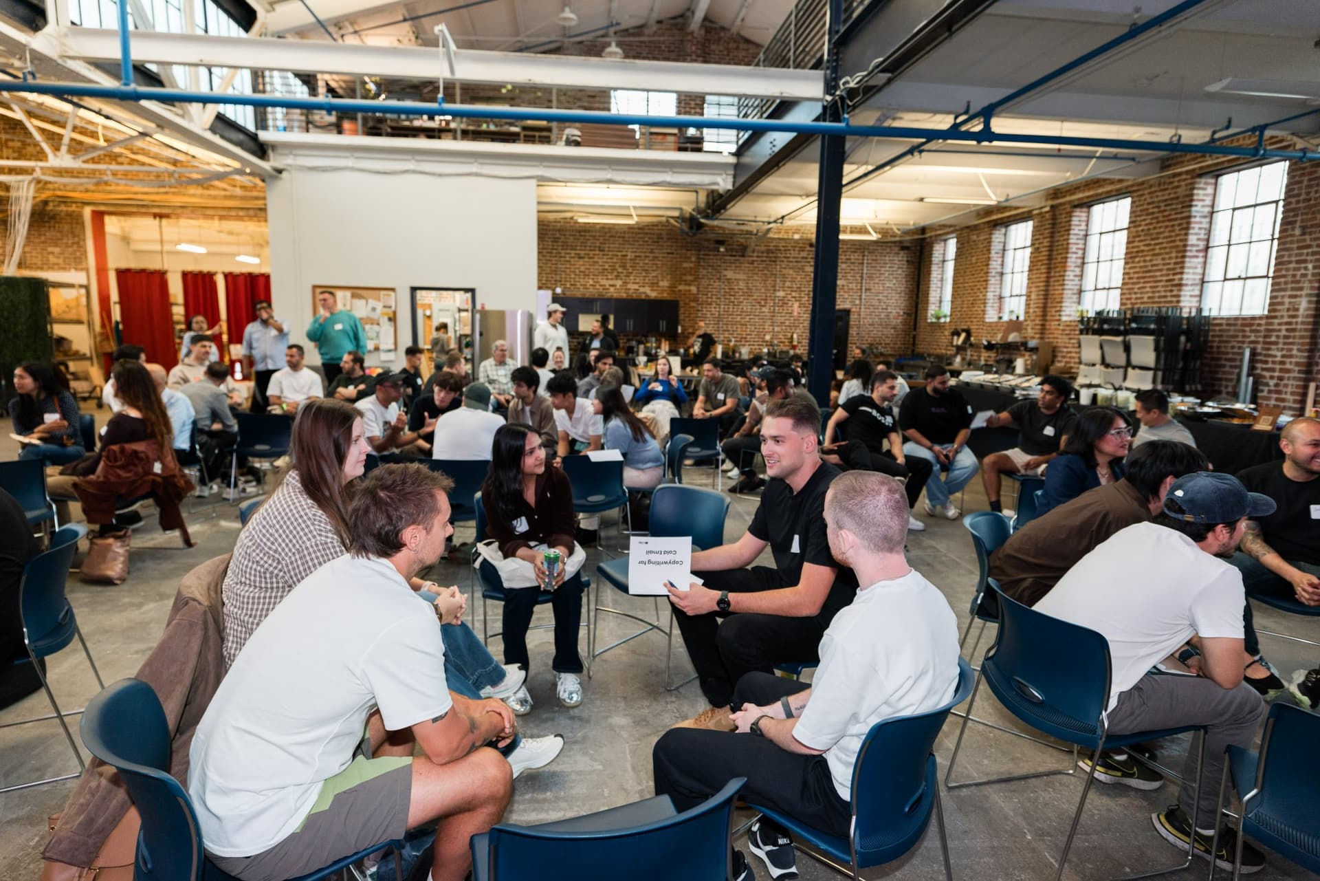 Attendees in small-group discussion circles across the room at Clay's Breaking the Mold community networking event during SF Tech Week 2026 in San Francisco by JY Studio