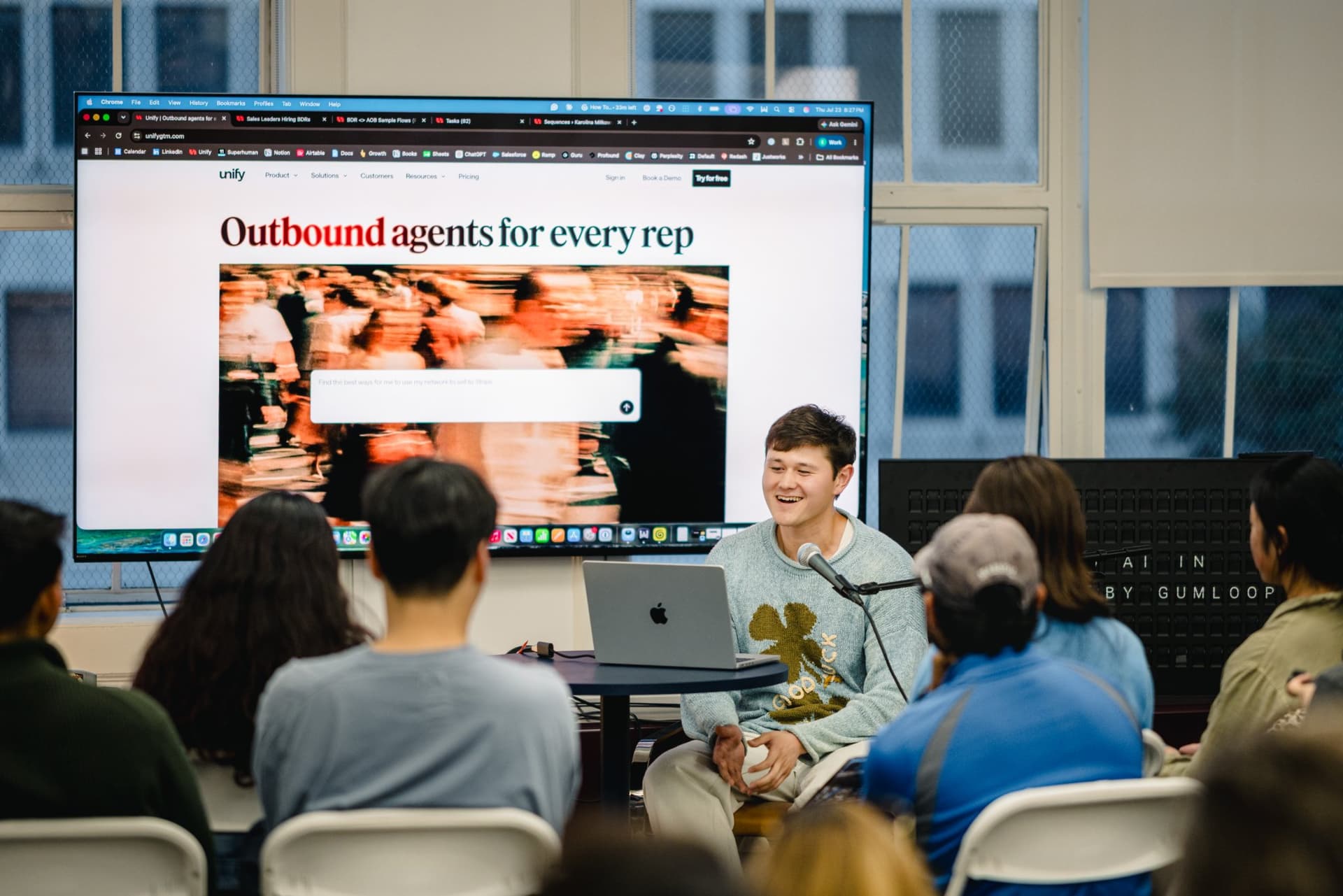 Speaker gesturing toward the screen while explaining an AI marketing workflow at Gumloop San Francisco