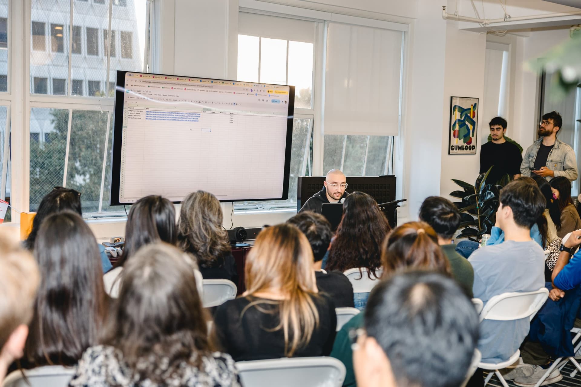 Speaker reviewing a content and SEO workflow spreadsheet on screen at the Gumloop event in San Francisco