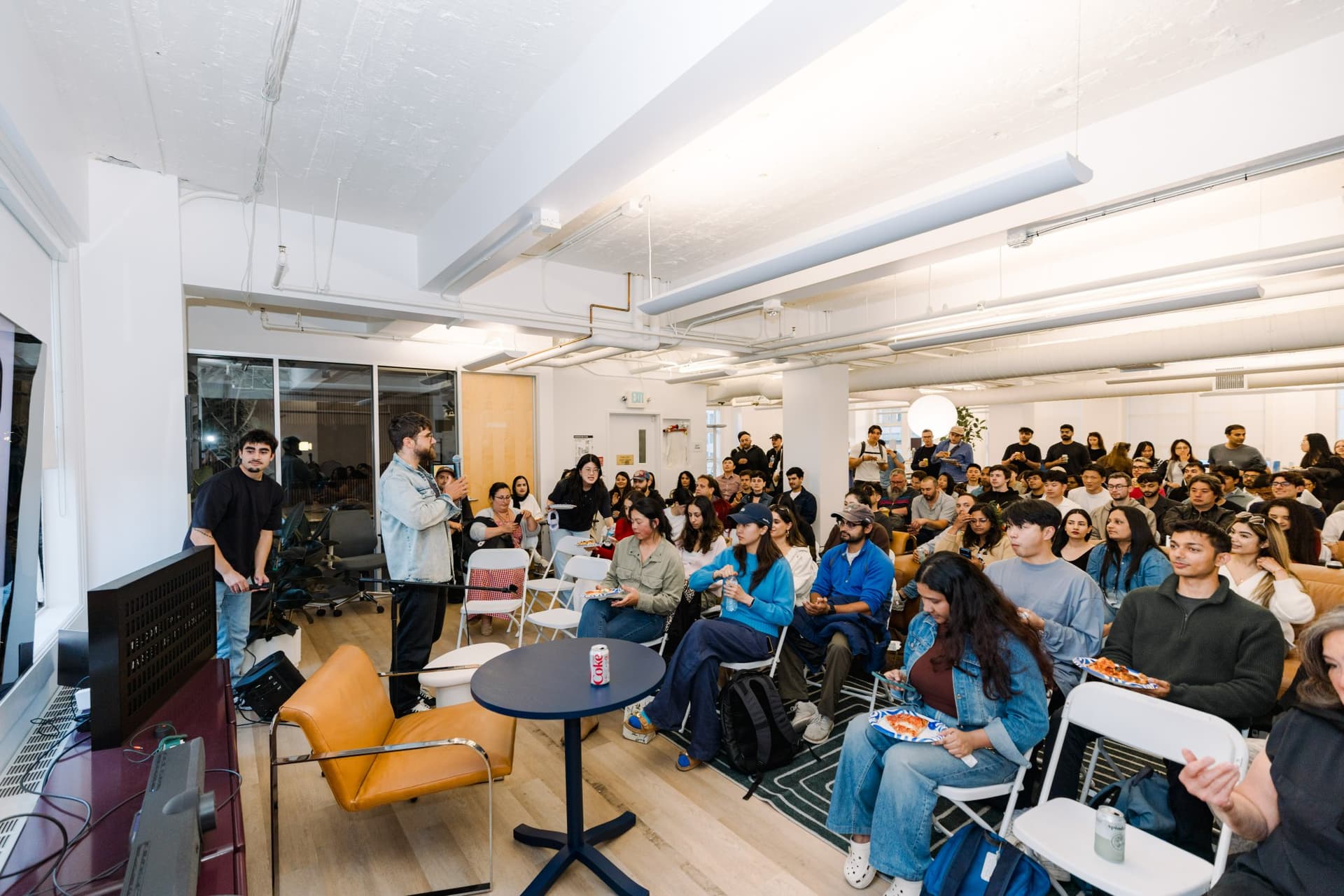 Wide shot of the packed room with guests holding pizza and drinks during Q&A at Gumloop's San Francisco office