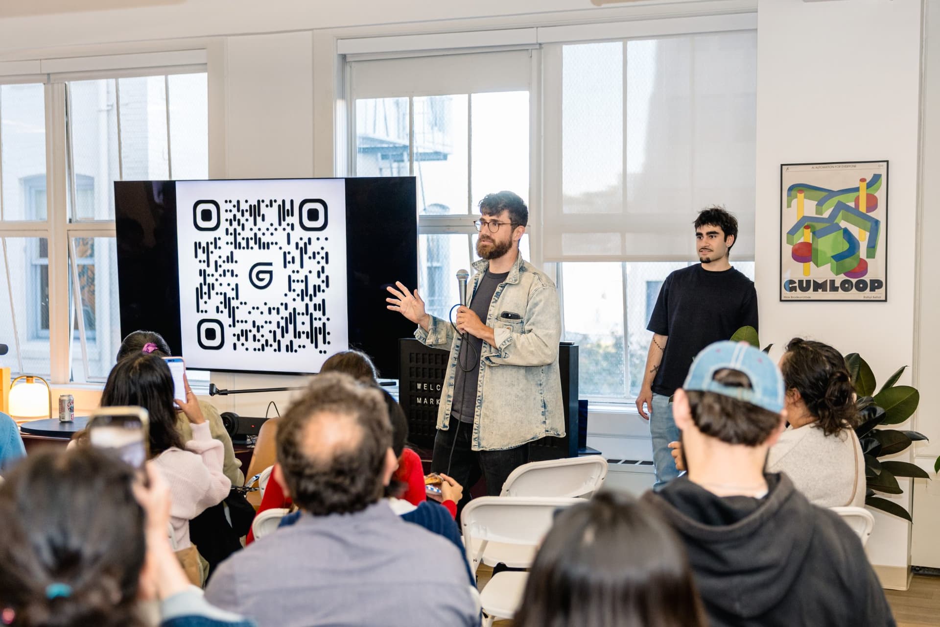 Host standing near the branded signage addressing the full room at the Gumloop meetup in San Francisco