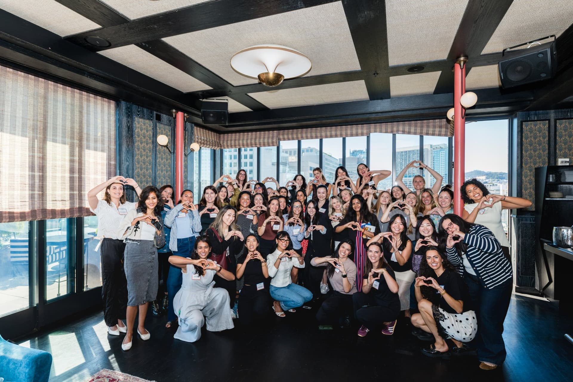 Group photo of women founders, builders, and operators making heart hands in the sunlit dining room at Lovable x Wispr Flow's Built on Her Terms brunch roundtable during SF Tech Week 2026 in San Francisco by JY Studio