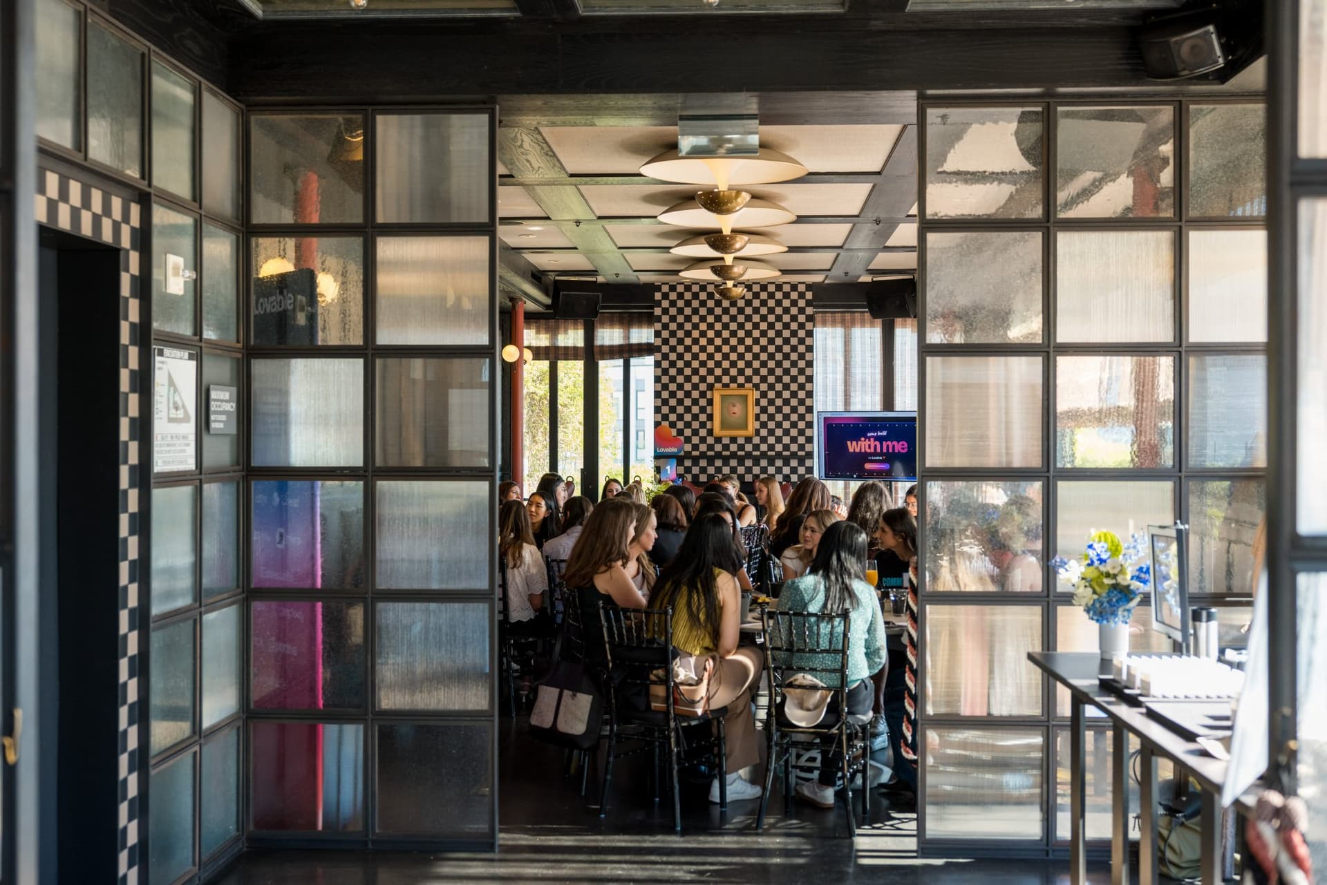 View through the glass doors into the dining room as guests settle into brunch tables at Lovable x Wispr Flow's Built on Her Terms brunch roundtable during SF Tech Week 2026 in San Francisco by JY Studio