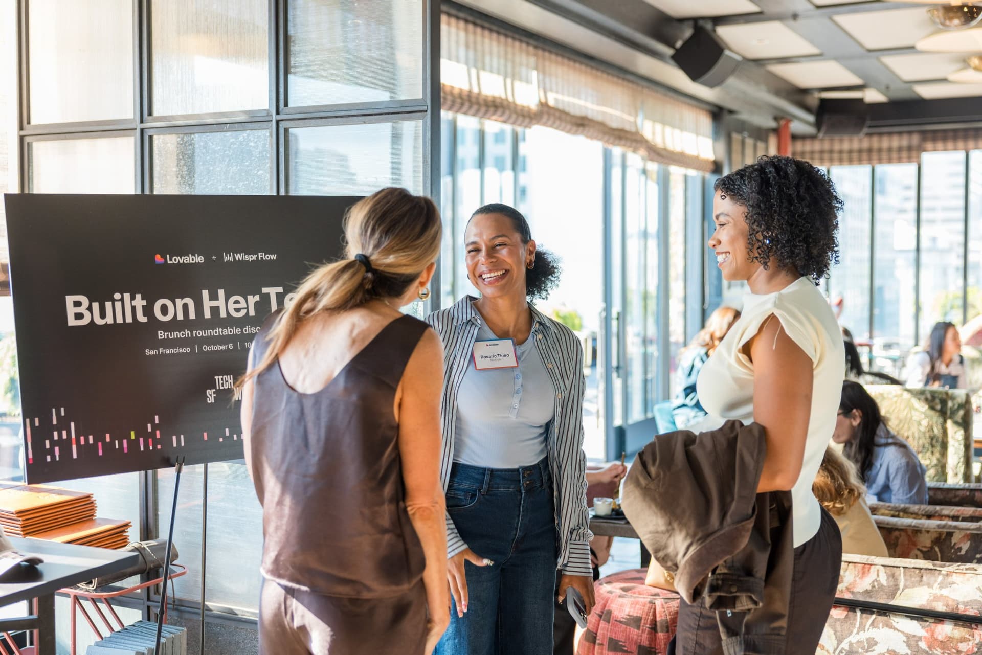 Guests greeting each other beside the Built on Her Terms event sign at Lovable x Wispr Flow's Built on Her Terms brunch roundtable during SF Tech Week 2026 in San Francisco by JY Studio
