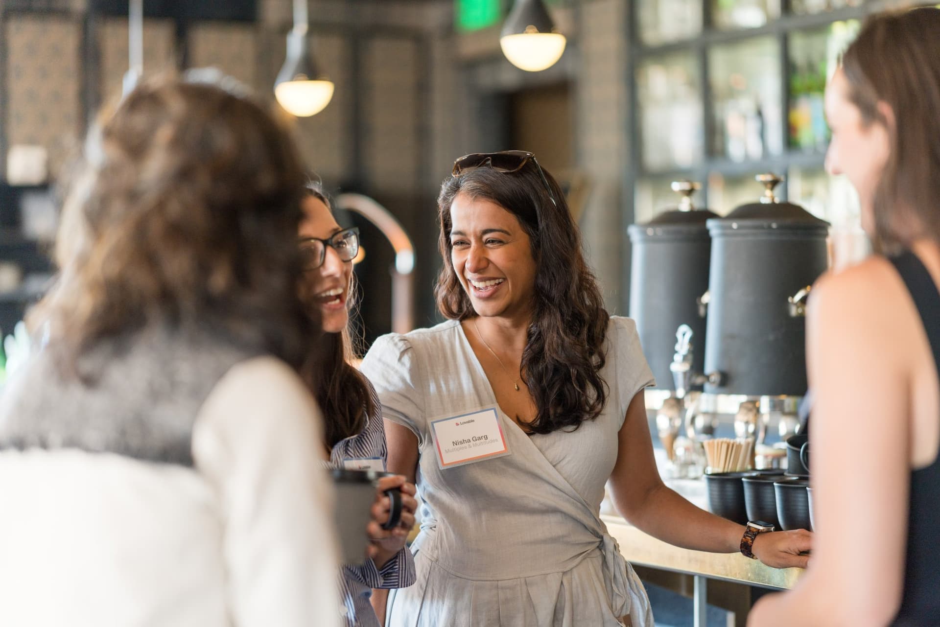 Women laughing and catching up by the coffee station with name tags on at Lovable x Wispr Flow's Built on Her Terms brunch roundtable during SF Tech Week 2026 in San Francisco by JY Studio