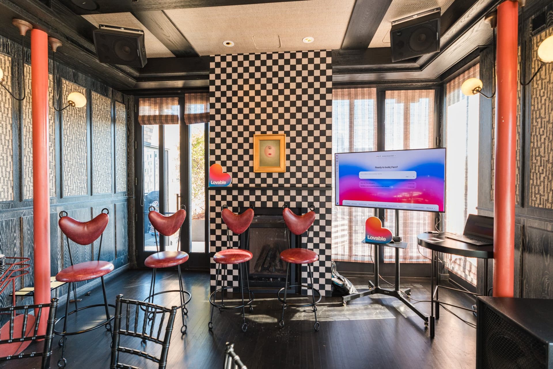 Checkerboard wall, red heart-back chairs, and welcome screen in the event space at Lovable x Wispr Flow's Built on Her Terms brunch roundtable during SF Tech Week 2026 in San Francisco by JY Studio