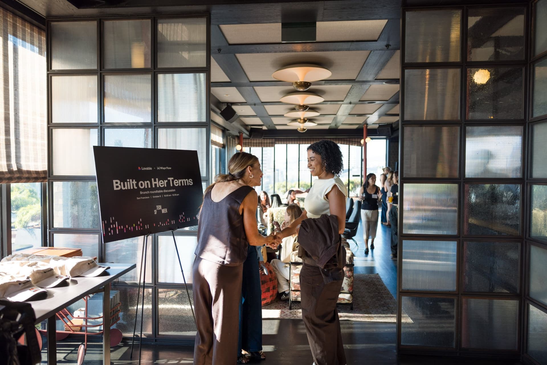 Guests arriving and greeting each other by the Built on Her Terms sign at Lovable x Wispr Flow's Built on Her Terms brunch roundtable during SF Tech Week 2026 in San Francisco by JY Studio