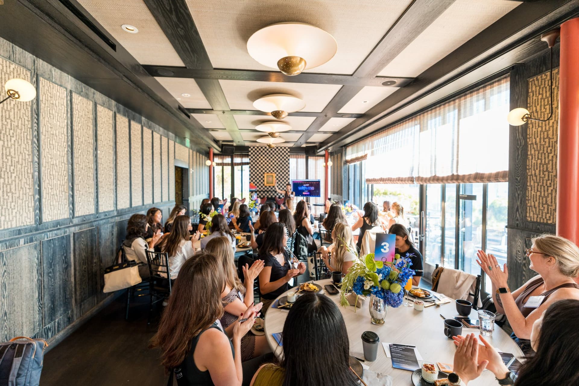 Wide view of the full dining room with every roundtable in conversation at Lovable x Wispr Flow's Built on Her Terms brunch roundtable during SF Tech Week 2026 in San Francisco by JY Studio