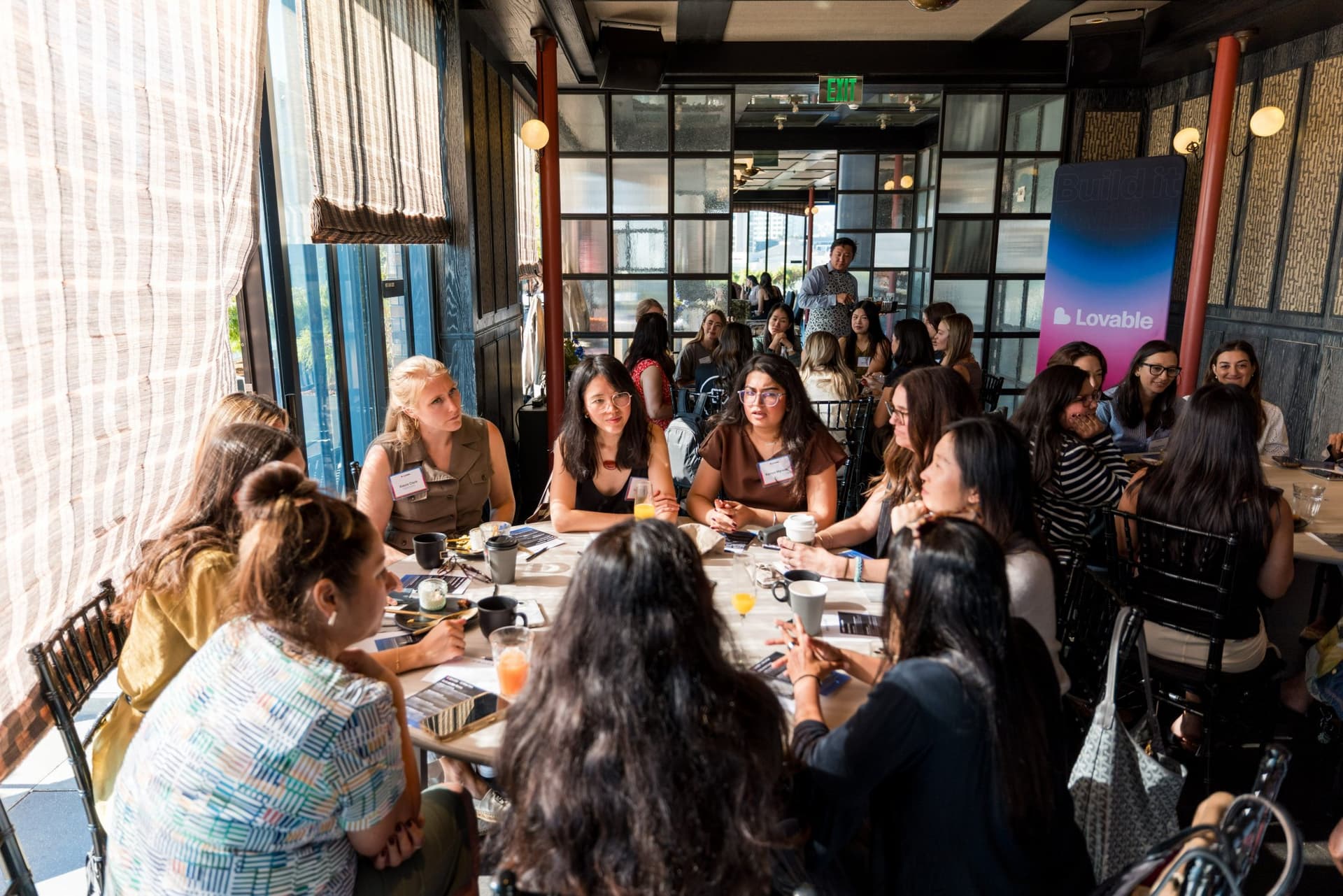 Women in tech talking at a brunch table beside the Lovable banner at Lovable x Wispr Flow's Built on Her Terms brunch roundtable during SF Tech Week 2026 in San Francisco by JY Studio