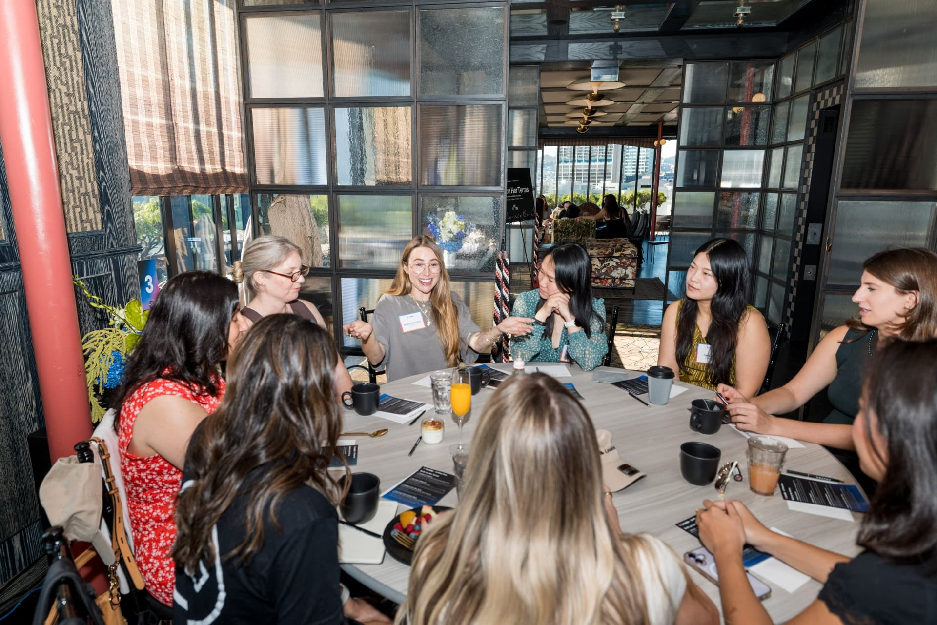 Roundtable guests leaning in to listen at a table by the window at Lovable x Wispr Flow's Built on Her Terms brunch roundtable during SF Tech Week 2026 in San Francisco by JY Studio