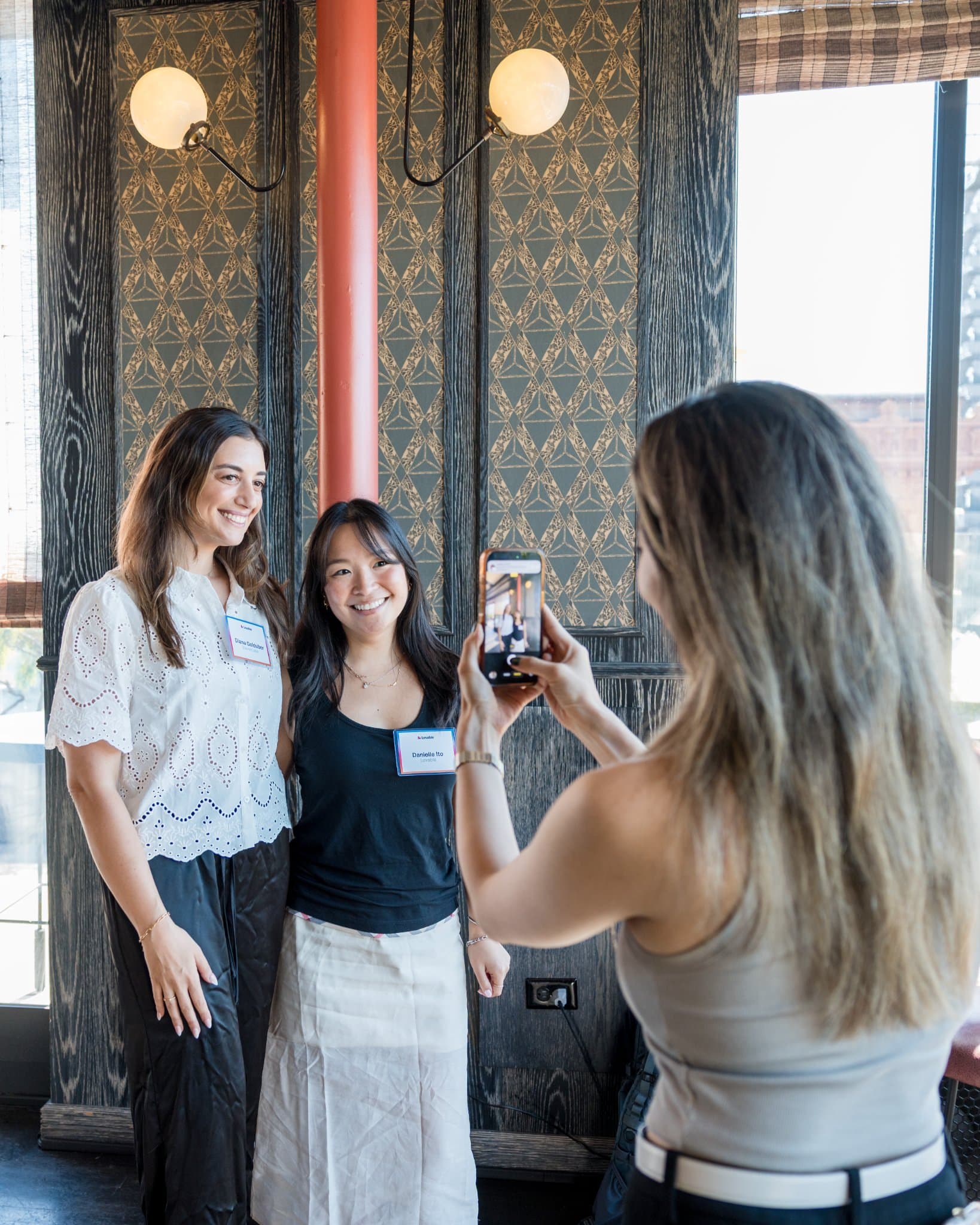 Guests posing for a phone photo against the patterned wall at Lovable x Wispr Flow's Built on Her Terms brunch roundtable during SF Tech Week 2026 in San Francisco by JY Studio