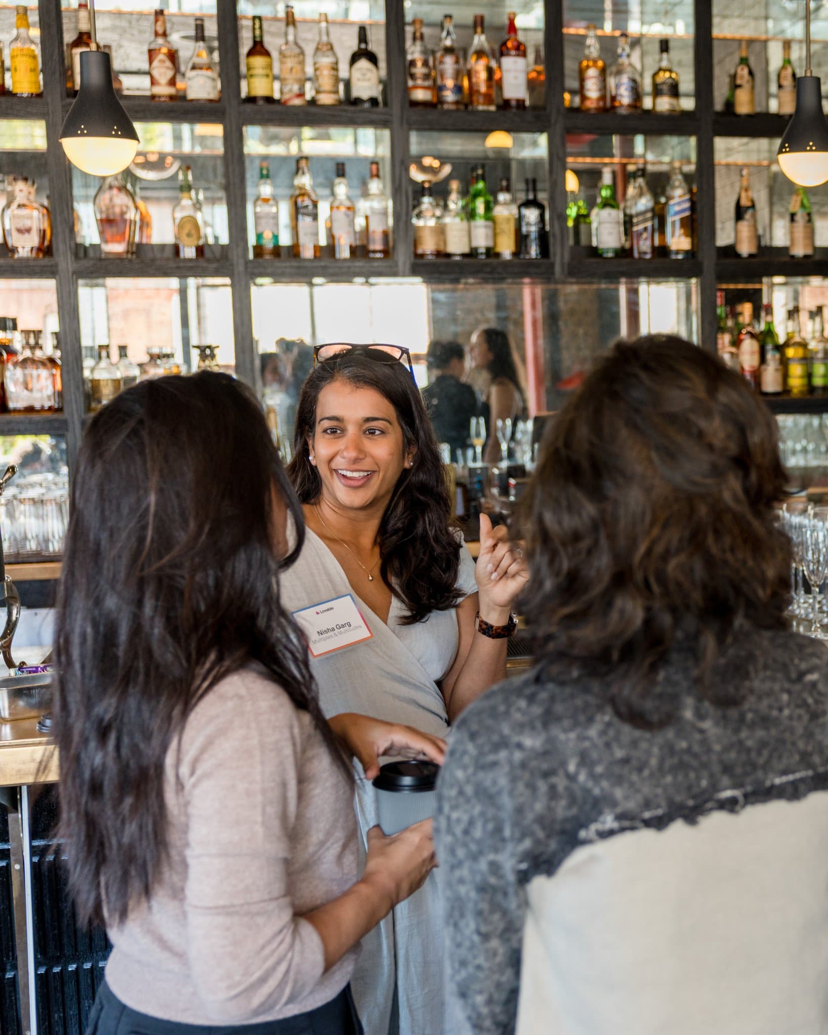 Guests chatting with coffee in front of the backlit bar at Lovable x Wispr Flow's Built on Her Terms brunch roundtable during SF Tech Week 2026 in San Francisco by JY Studio