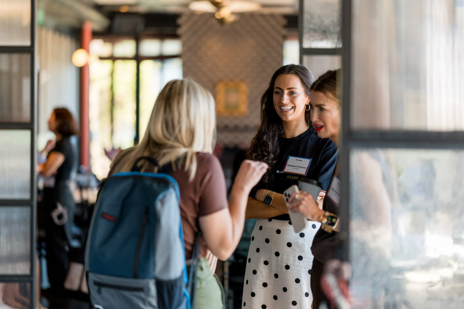 Guest smiling during a conversation near the event space entrance at Lovable x Wispr Flow's Built on Her Terms brunch roundtable during SF Tech Week 2026 in San Francisco by JY Studio