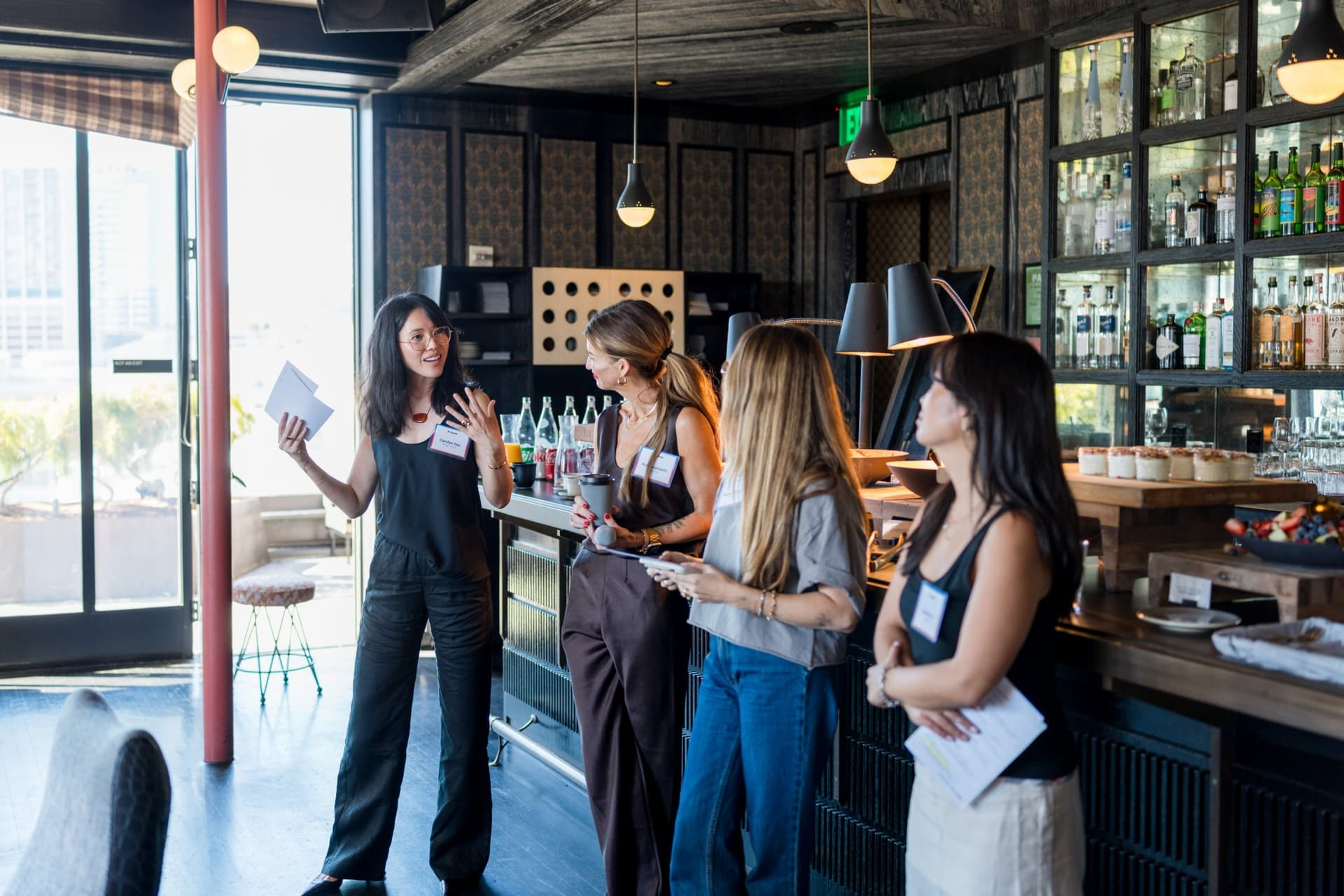 Hosts addressing guests from the bar during the closing share-out at Lovable x Wispr Flow's Built on Her Terms brunch roundtable during SF Tech Week 2026 in San Francisco by JY Studio