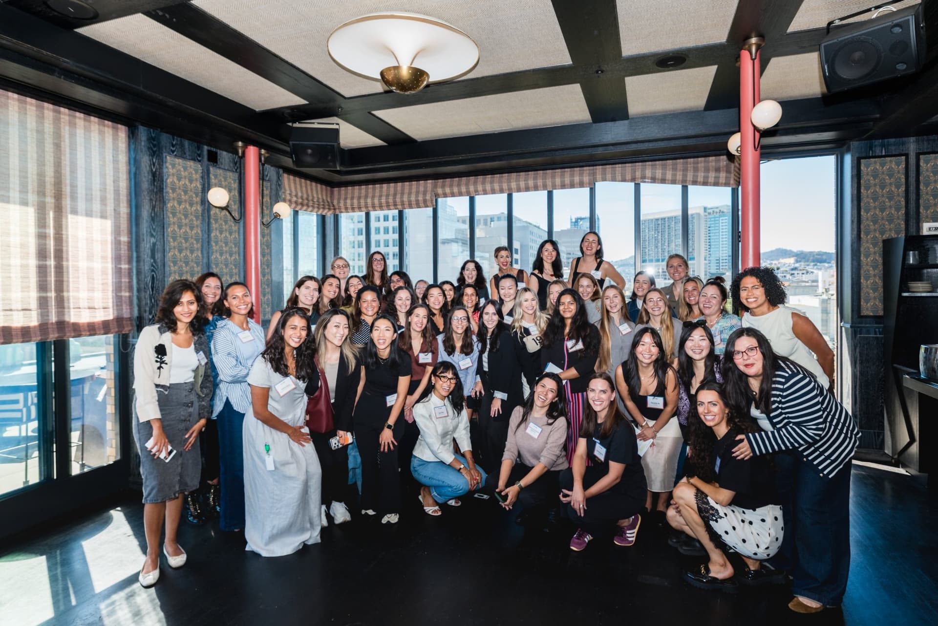 Group photo of all attendees in front of the San Francisco skyline windows at Lovable x Wispr Flow's Built on Her Terms brunch roundtable during SF Tech Week 2026 in San Francisco by JY Studio