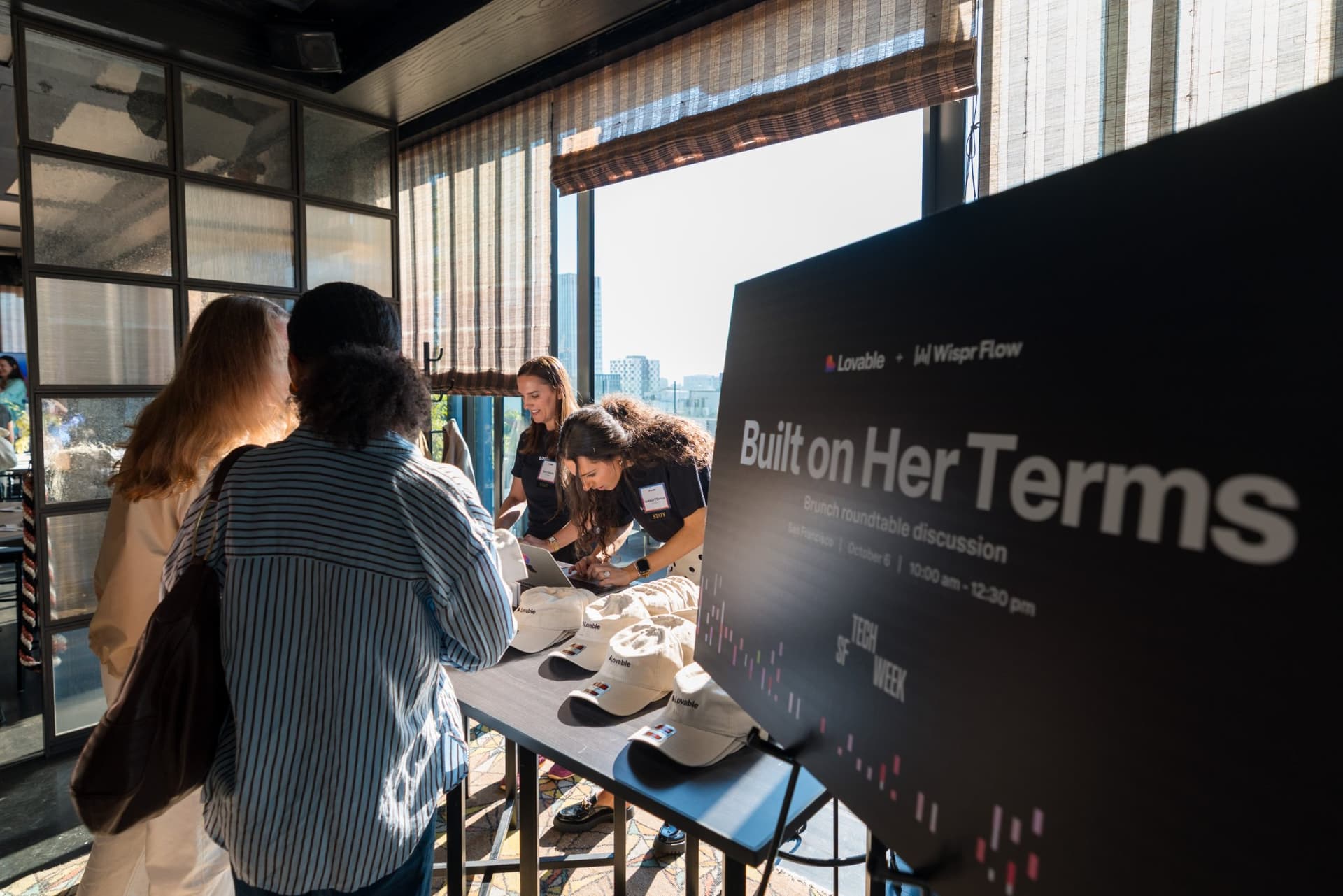 Guests browsing the Lovable merch table beside the Built on Her Terms sign at Lovable x Wispr Flow's Built on Her Terms brunch roundtable during SF Tech Week 2026 in San Francisco by JY Studio