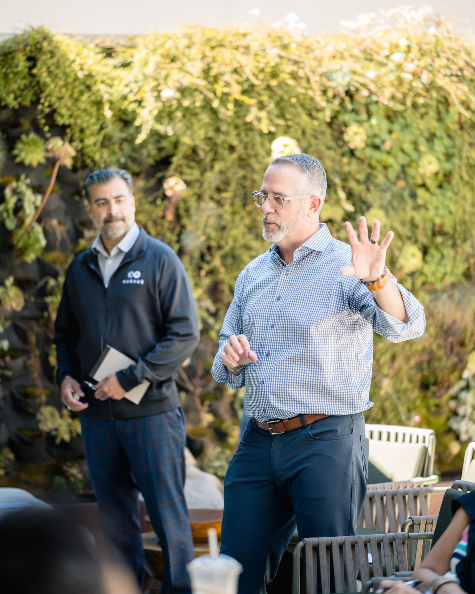 Speaker gesturing while addressing members near the living green wall at the Magnus event in Palo Alto