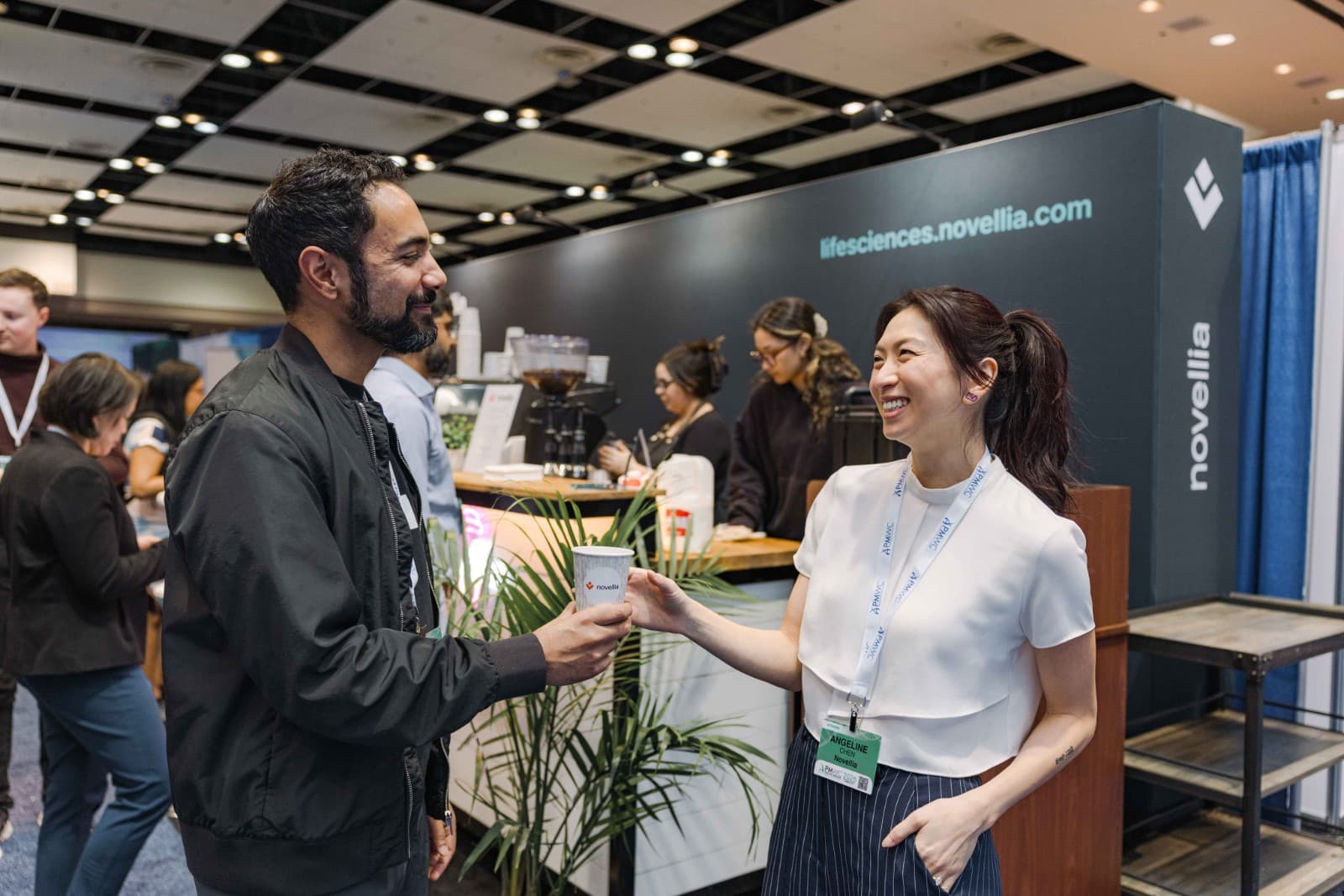 Attendees networking at Novellia exhibit during PMWC 2026 conference in Santa Clara Bay Area by JY Studio