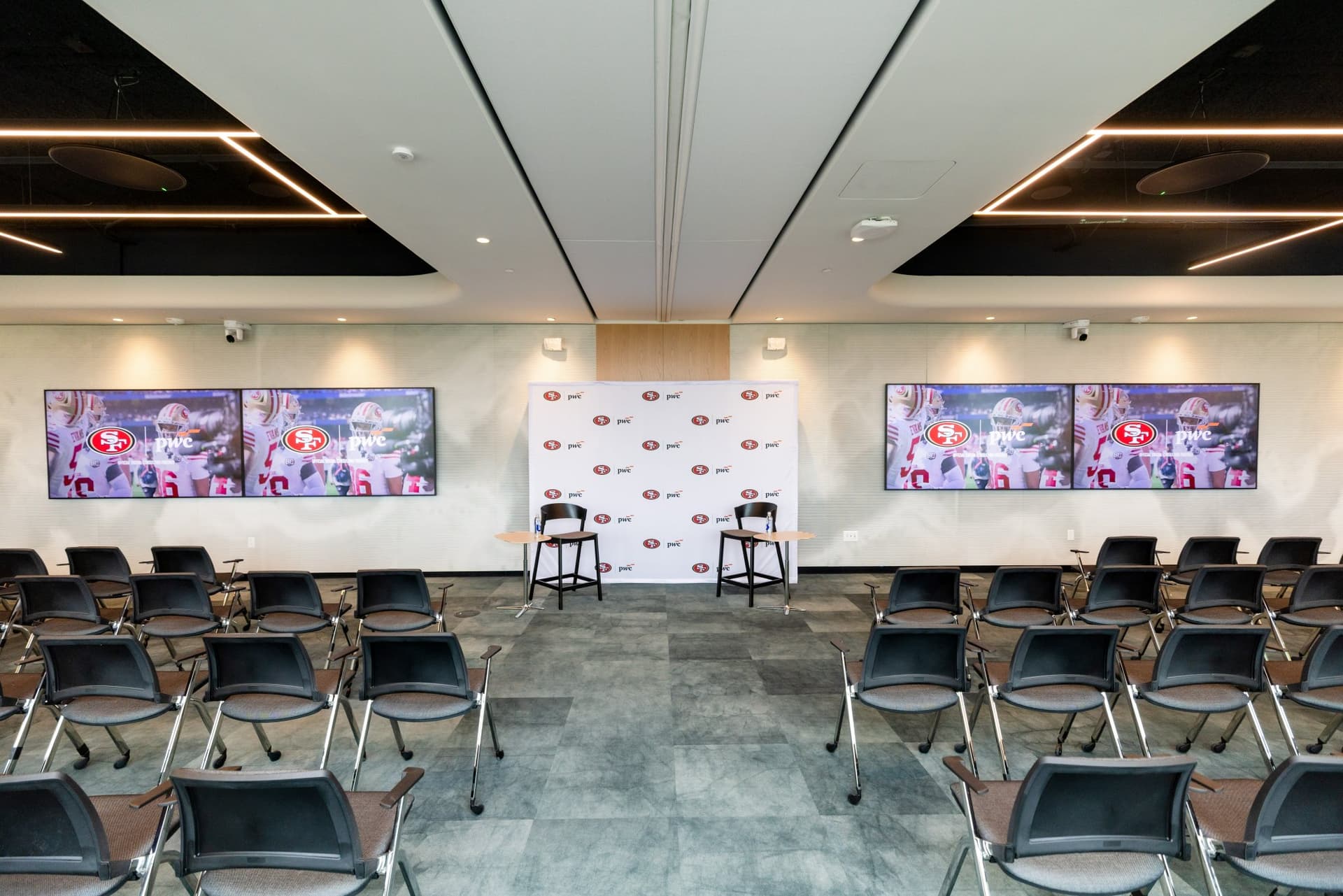 Event room set up with rows of chairs, 49ers highlight screens and the 49ers and PwC backdrop before guests arrive at the PwC x 49ers event at PwC Silicon Valley in San Jose by JY Studio