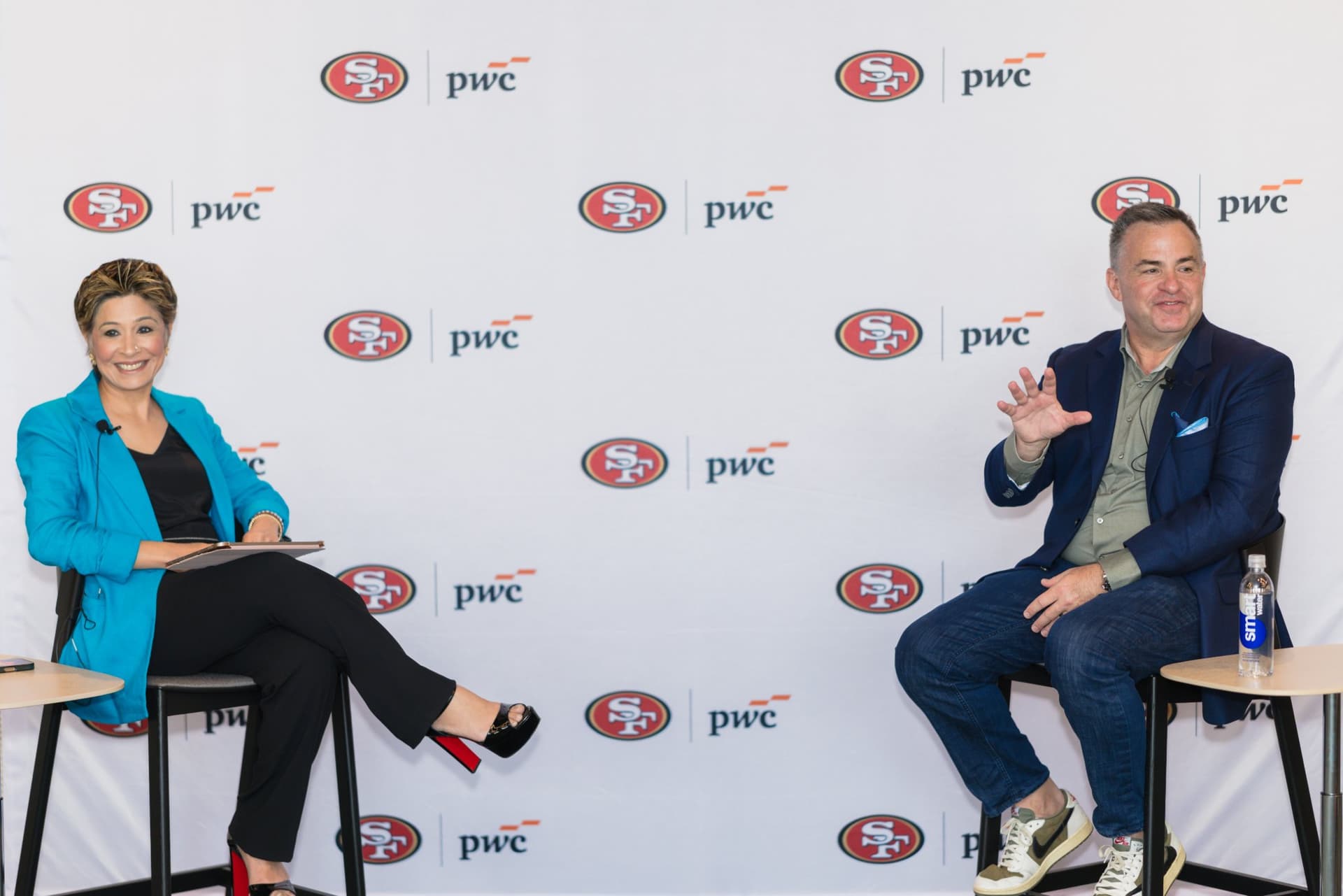 Moderator in a teal blazer and guest speaker in conversation in front of the 49ers and PwC step-and-repeat at the PwC x 49ers event at PwC Silicon Valley in San Jose by JY Studio