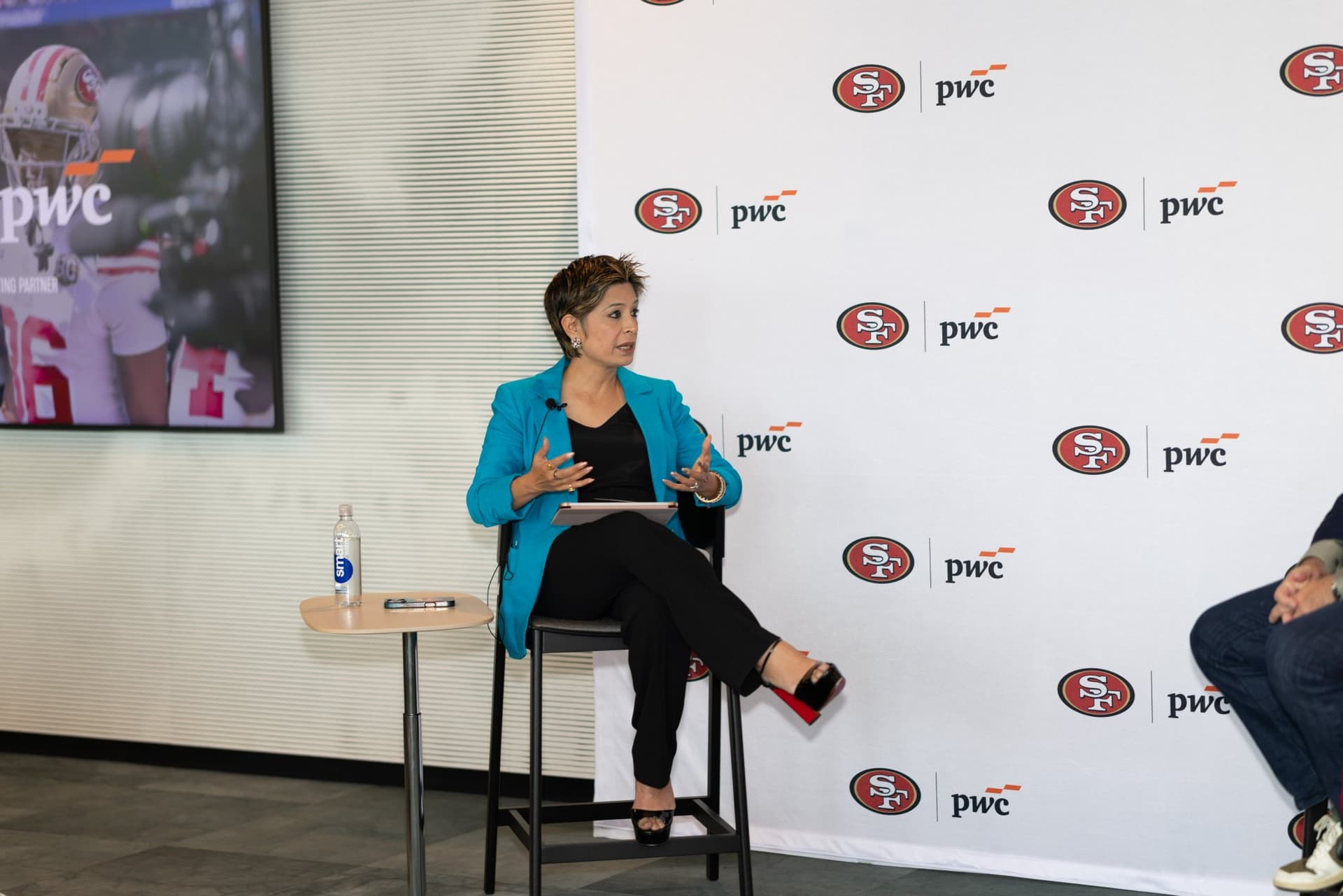 Moderator in a teal blazer asking questions during the fireside chat at the PwC x 49ers event at PwC Silicon Valley in San Jose by JY Studio