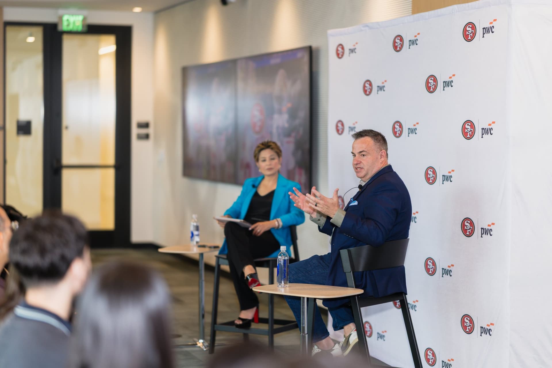 Guest speaker and moderator in conversation beside a 49ers highlight screen at the PwC x 49ers event at PwC Silicon Valley in San Jose by JY Studio