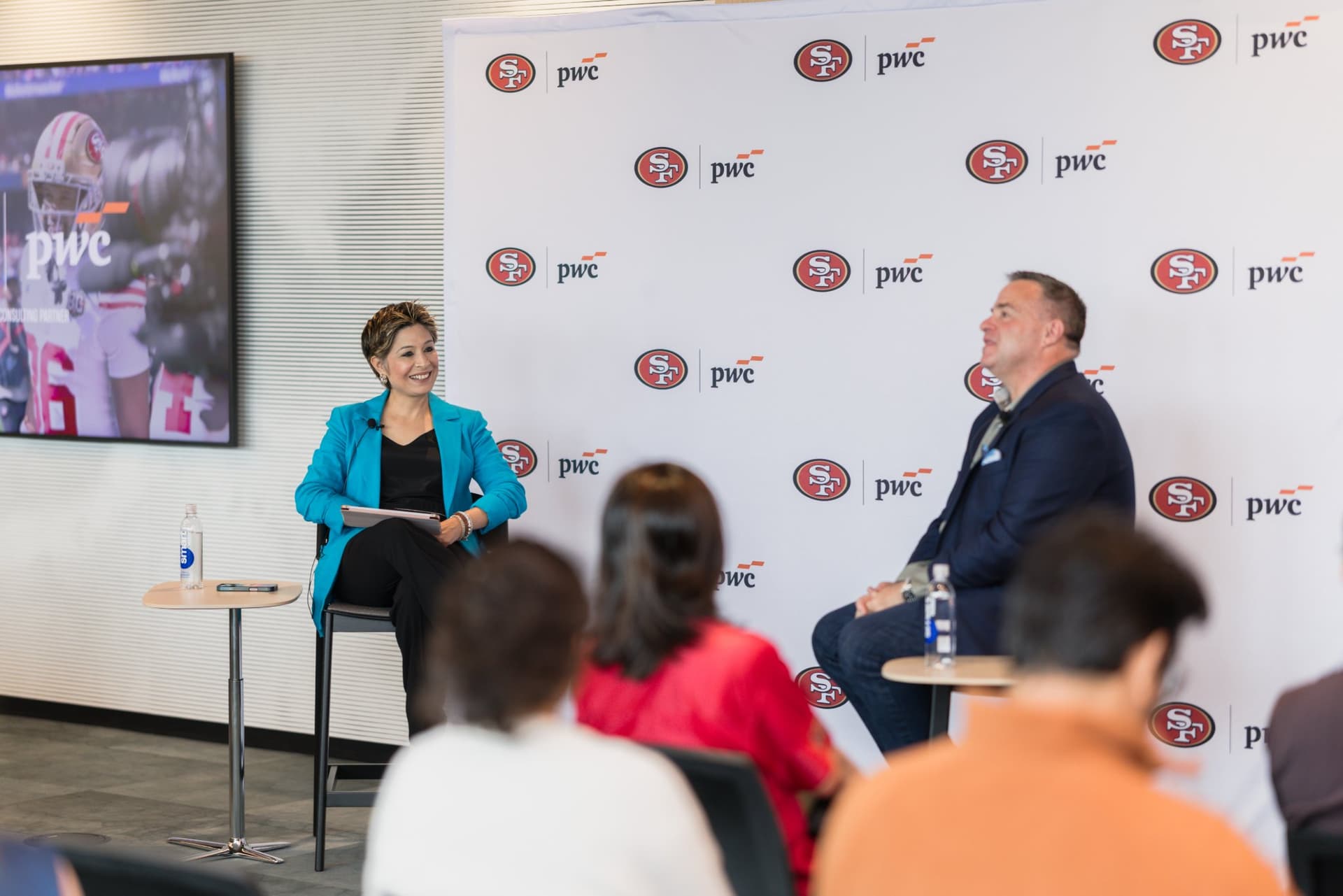 Moderator and guest speaker on stage seen over the heads of the audience at the PwC x 49ers event at PwC Silicon Valley in San Jose by JY Studio