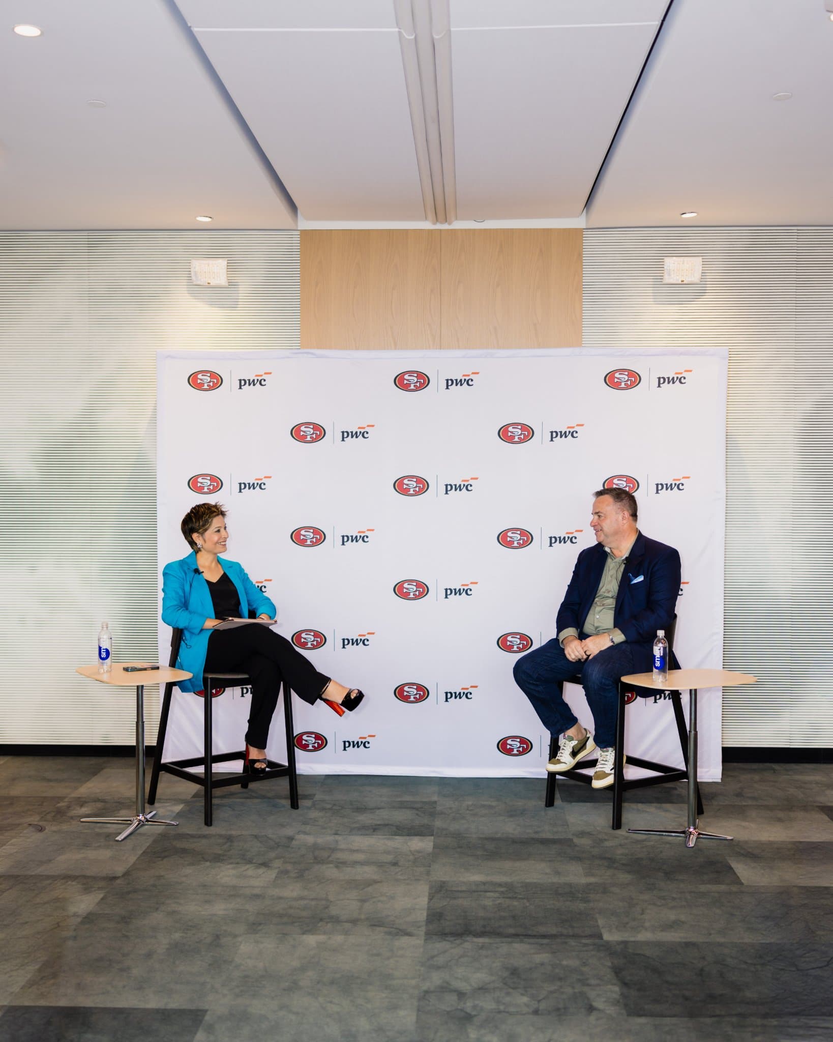 Full stage view of the moderator and guest speaker in front of the 49ers and PwC backdrop at the PwC x 49ers event at PwC Silicon Valley in San Jose by JY Studio