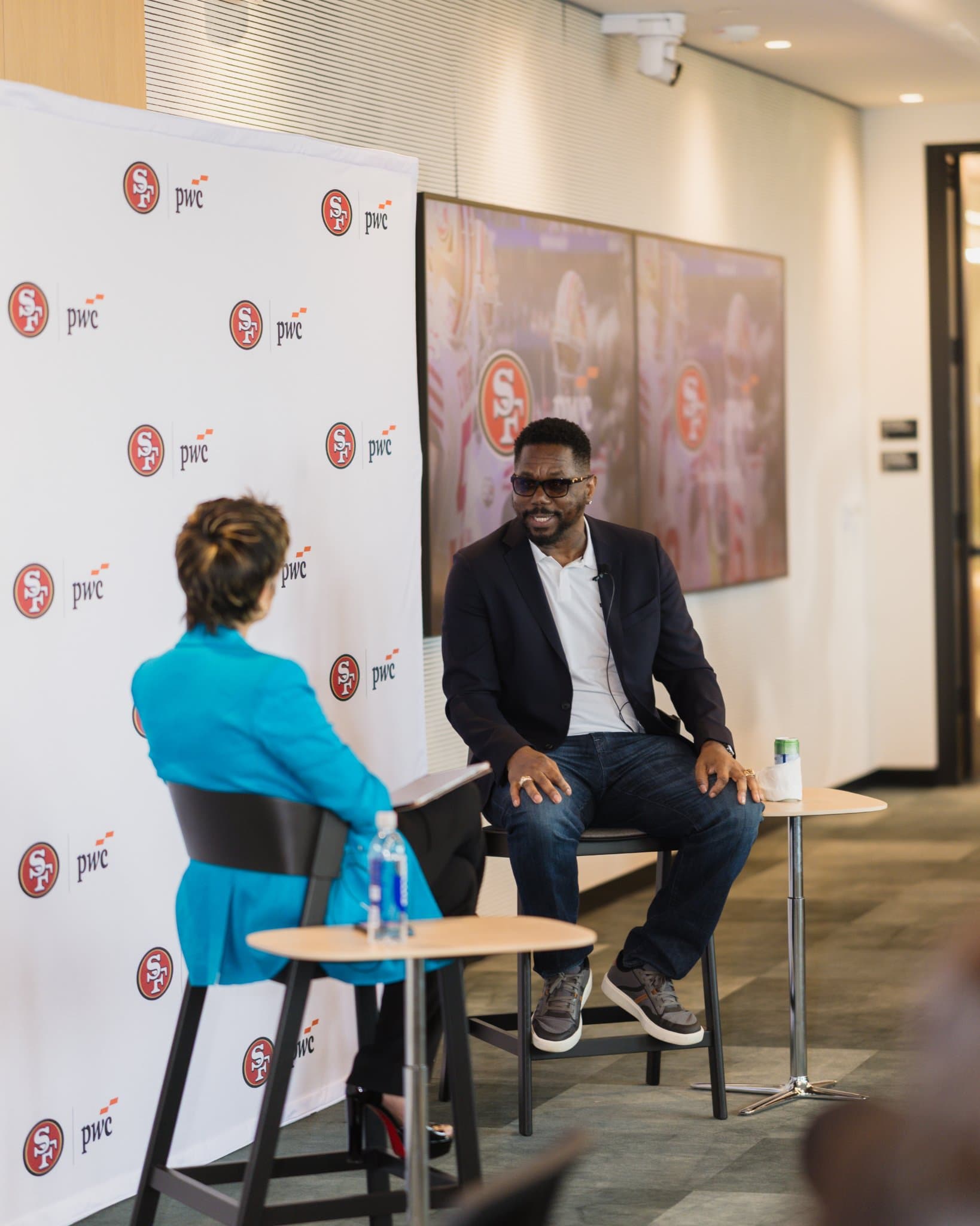 49ers legend speaking with the moderator in front of 49ers highlight screens at the PwC x 49ers event at PwC Silicon Valley in San Jose by JY Studio