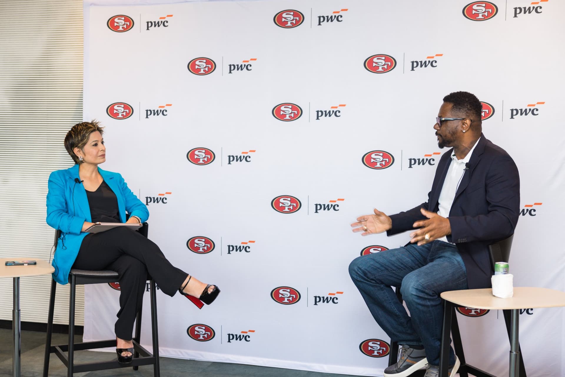 Moderator and 49ers legend in conversation in front of the 49ers and PwC backdrop at the PwC x 49ers event at PwC Silicon Valley in San Jose by JY Studio
