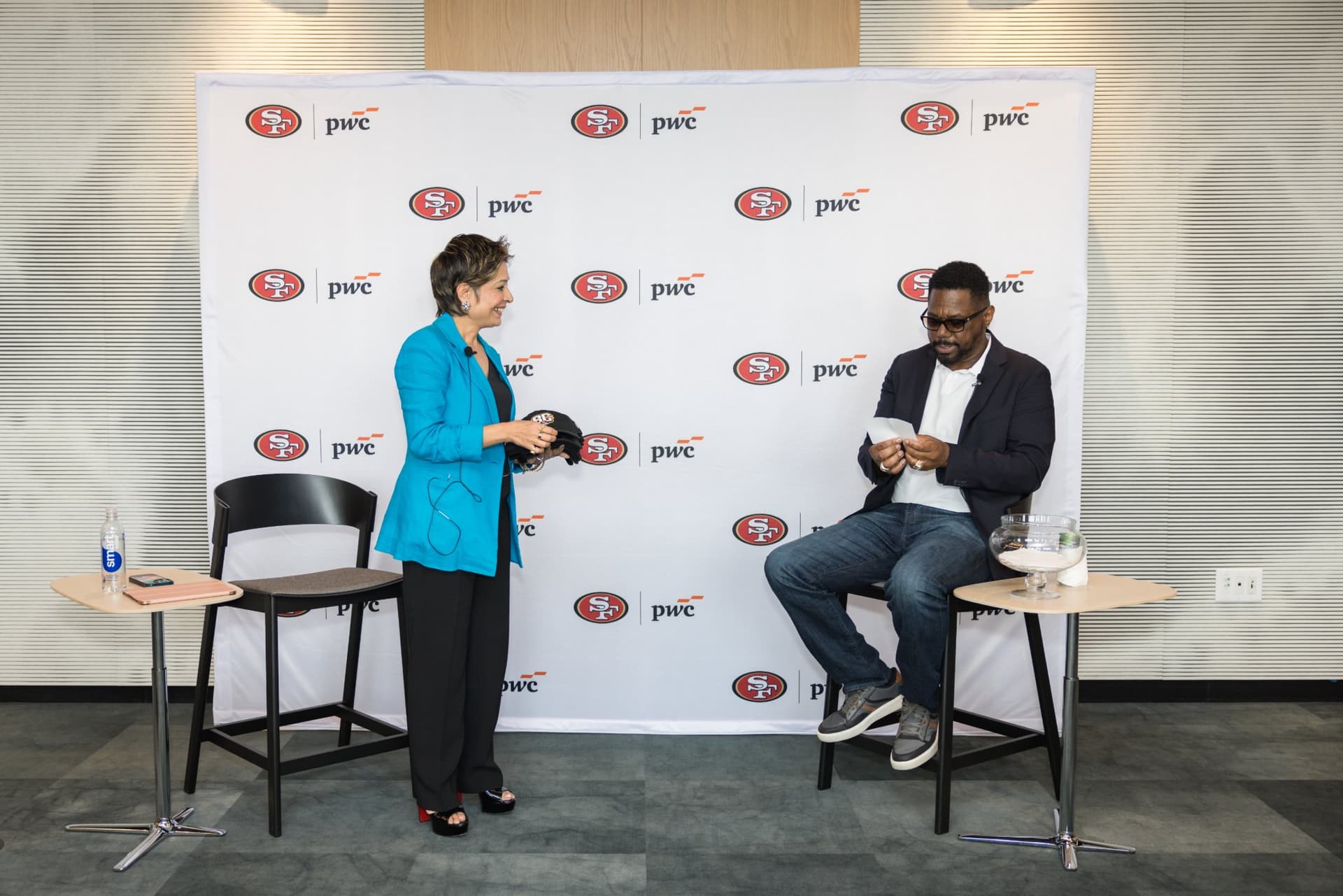 Moderator holding 49ers caps as the 49ers legend reads raffle cards for the giveaway at the PwC x 49ers event at PwC Silicon Valley in San Jose by JY Studio