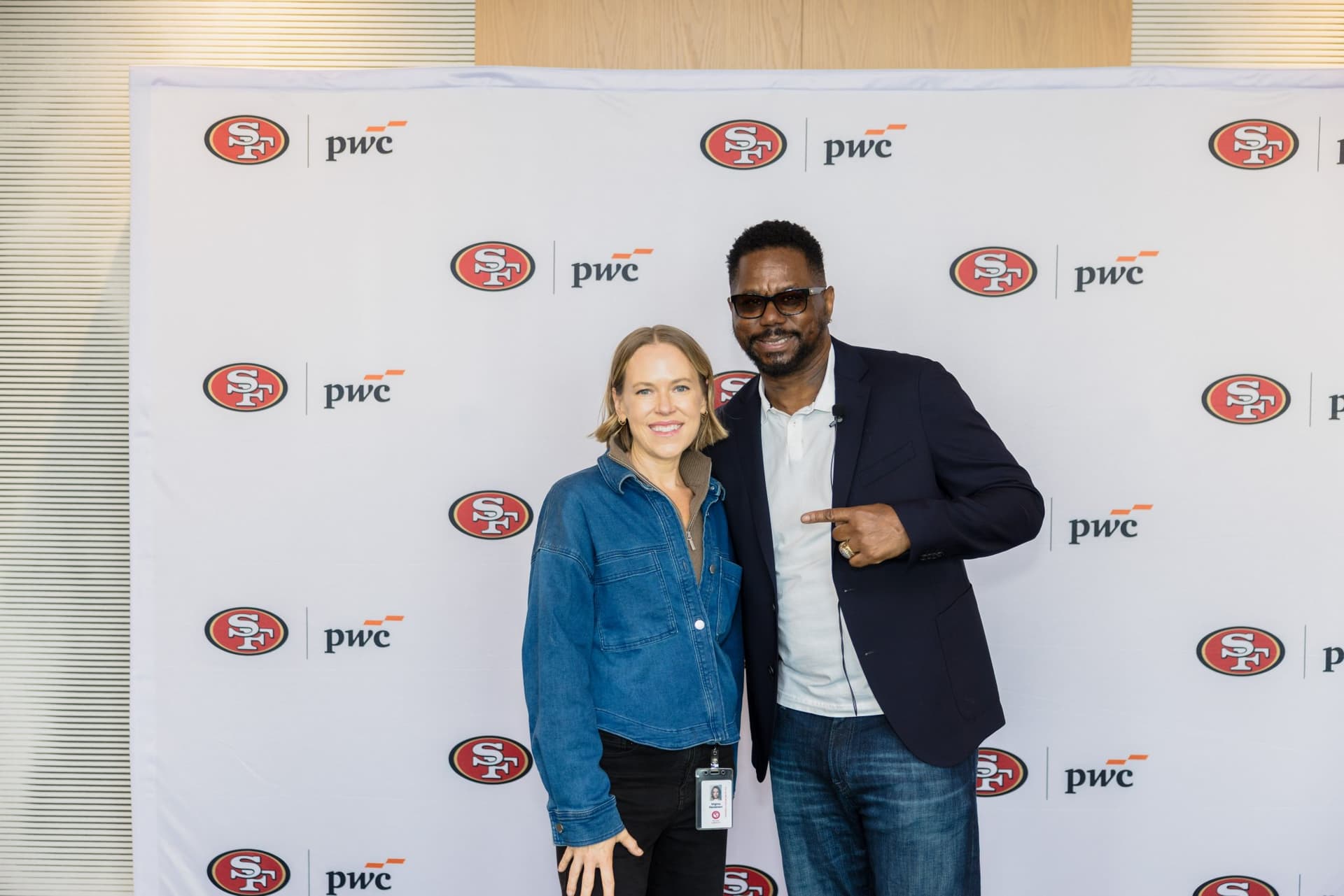 Attendee posing with the 49ers legend as he points to her at the step-and-repeat at the PwC x 49ers event at PwC Silicon Valley in San Jose by JY Studio