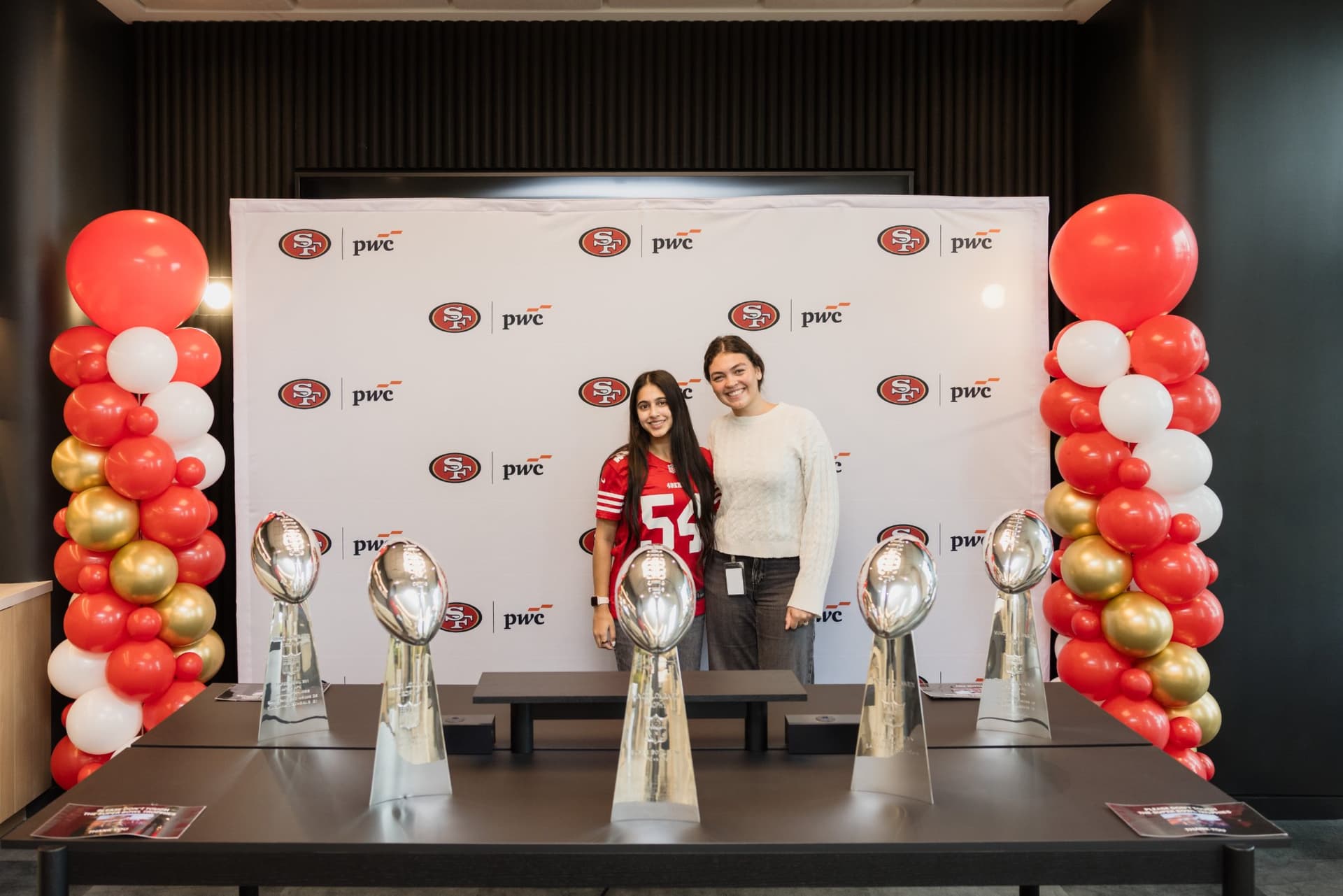 Attendees posing behind the five Super Bowl Lombardi Trophies at the 49ers and PwC backdrop at the PwC x 49ers event at PwC Silicon Valley in San Jose by JY Studio