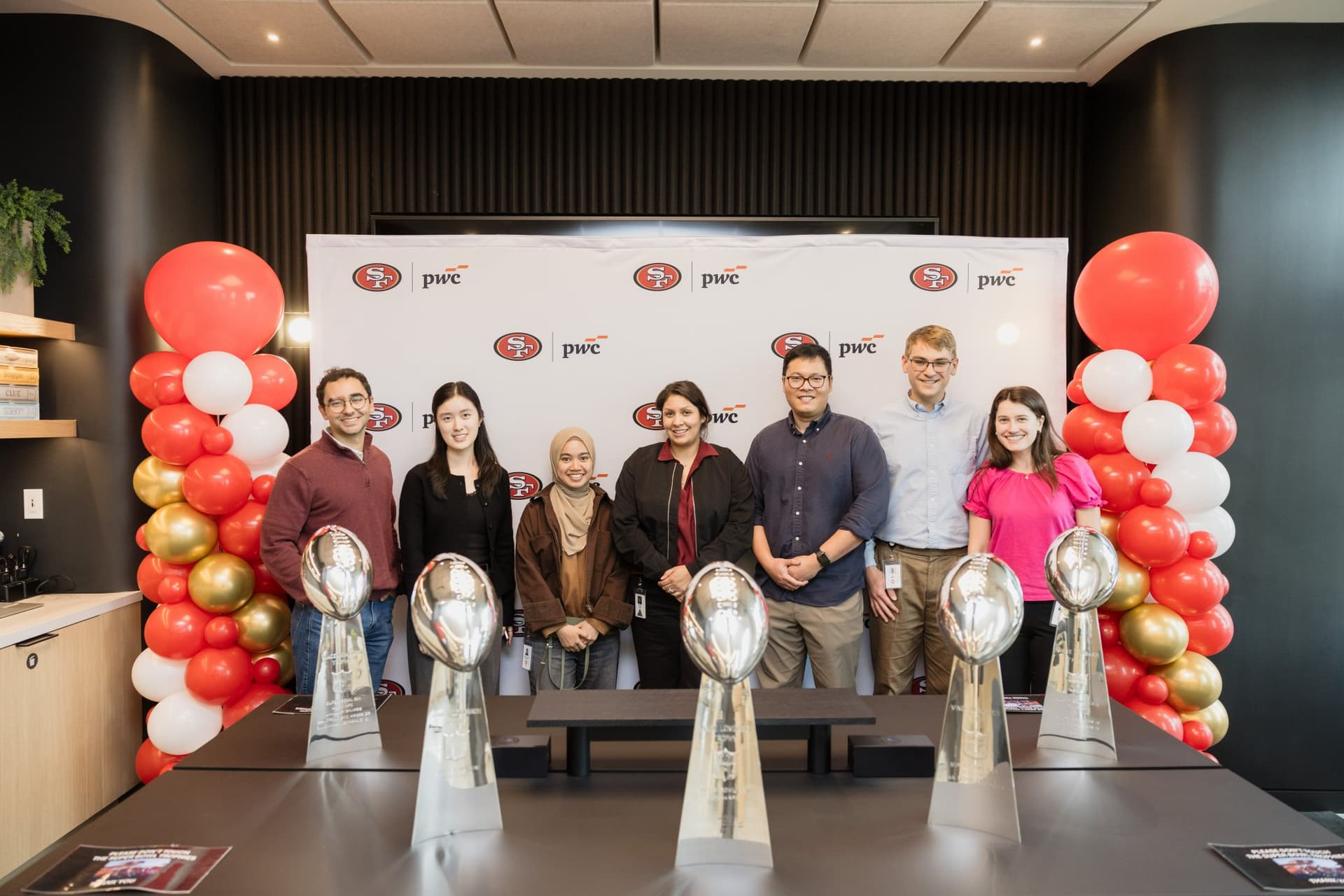 PwC team members posing behind the five Super Bowl Lombardi Trophies with balloon columns at the PwC x 49ers event at PwC Silicon Valley in San Jose by JY Studio