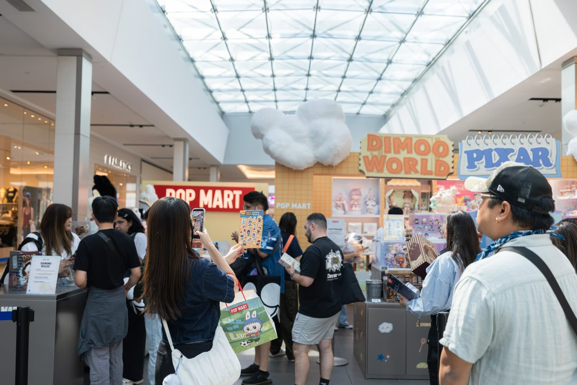 Crowd of Pop Mart fans around the DIMOO WORLD x PIXAR pop-up booth under the Valley Fair skylight at the Pop Mart DIMOO WORLD x PIXAR pop-up at Westfield Valley Fair in Santa Clara by JY Studio