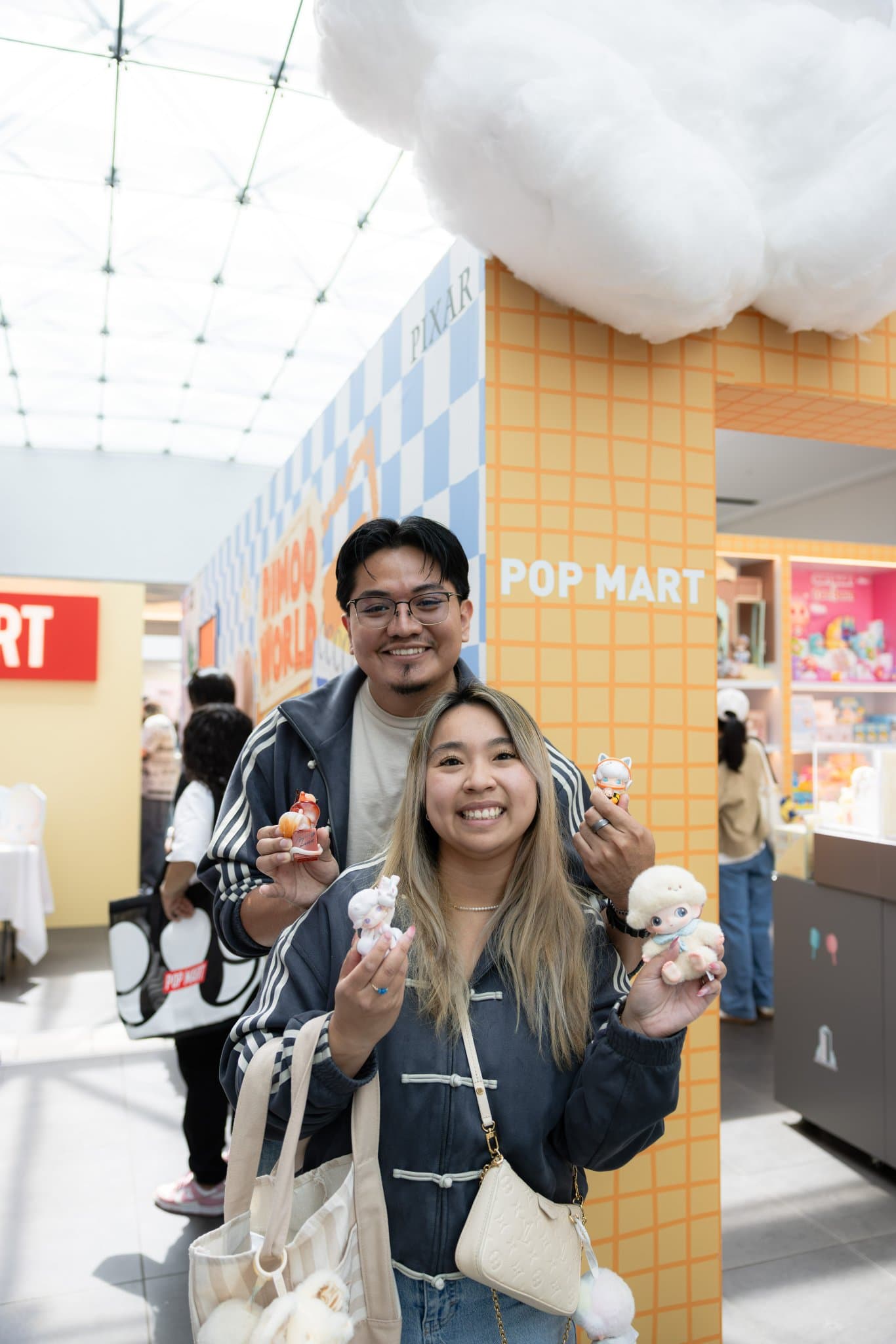 Couple posing with their DIMOO blind box figures at the Pop Mart DIMOO WORLD x PIXAR pop-up at Westfield Valley Fair in Santa Clara by JY Studio