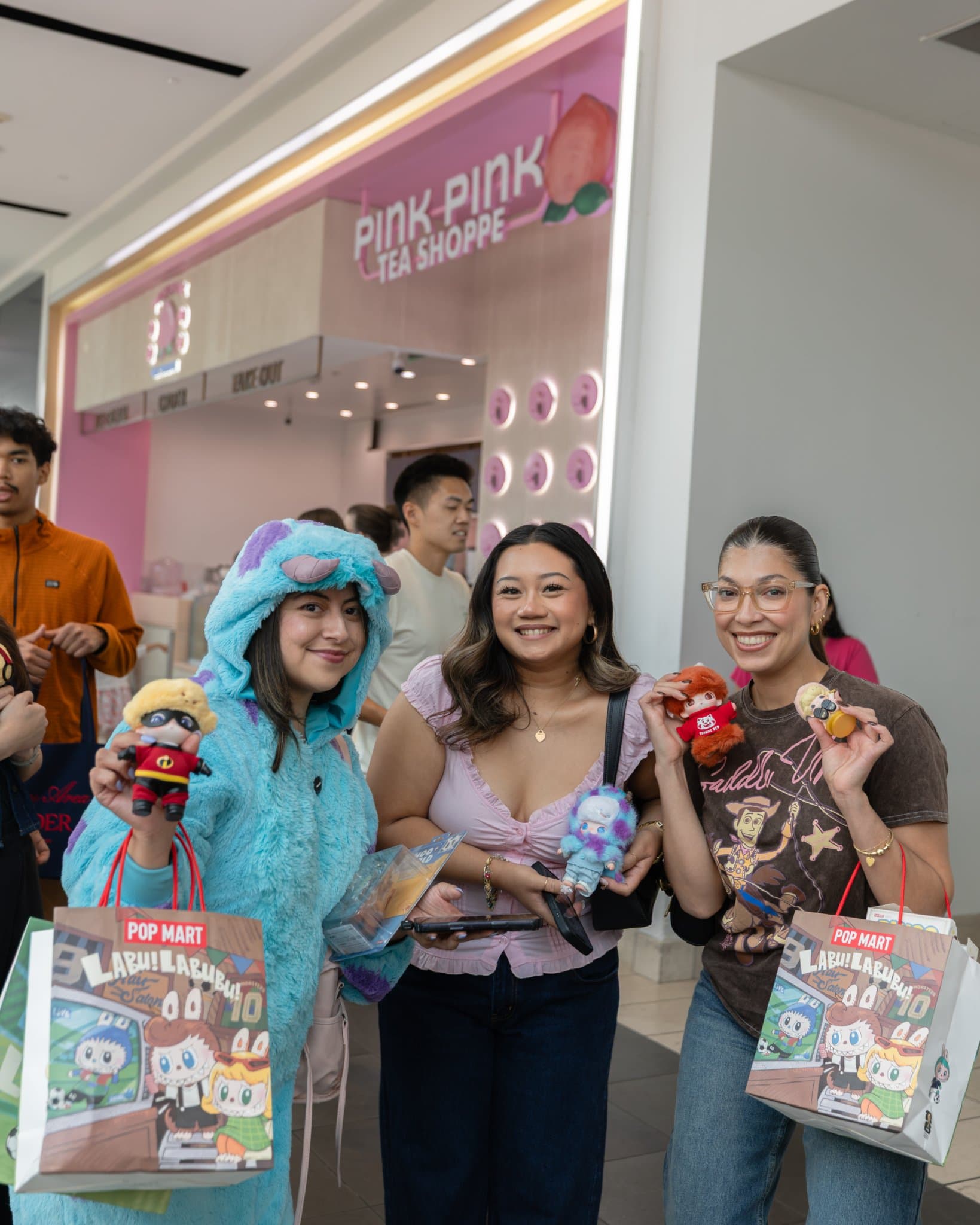 Three friends in costume holding DIMOO figures and Pop Mart shopping bags at the Pop Mart DIMOO WORLD x PIXAR pop-up at Westfield Valley Fair in Santa Clara by JY Studio