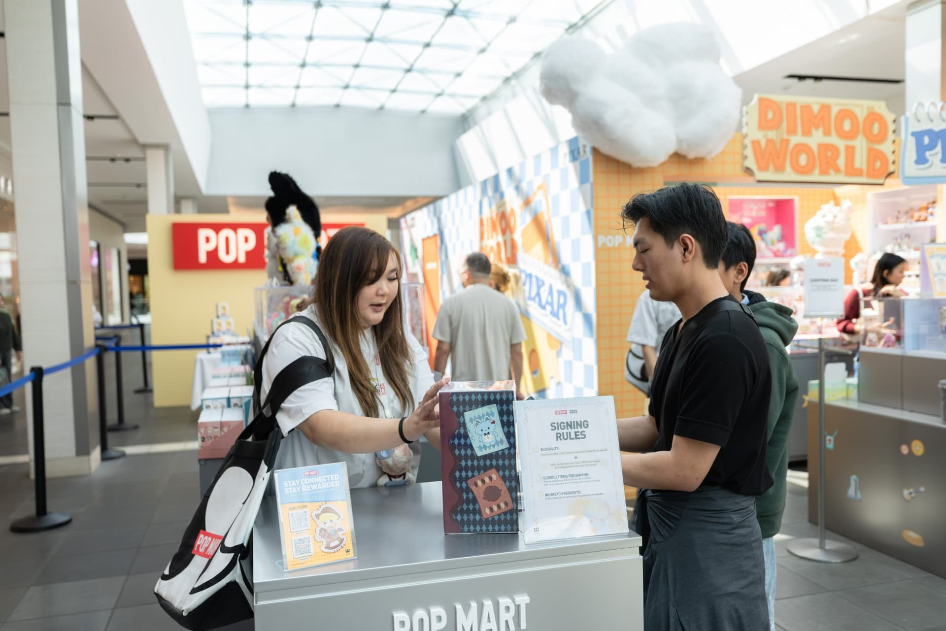 Pop Mart staff helping collectors at the DIMOO WORLD x PIXAR pop-up checkout counter at the Pop Mart DIMOO WORLD x PIXAR pop-up at Westfield Valley Fair in Santa Clara by JY Studio